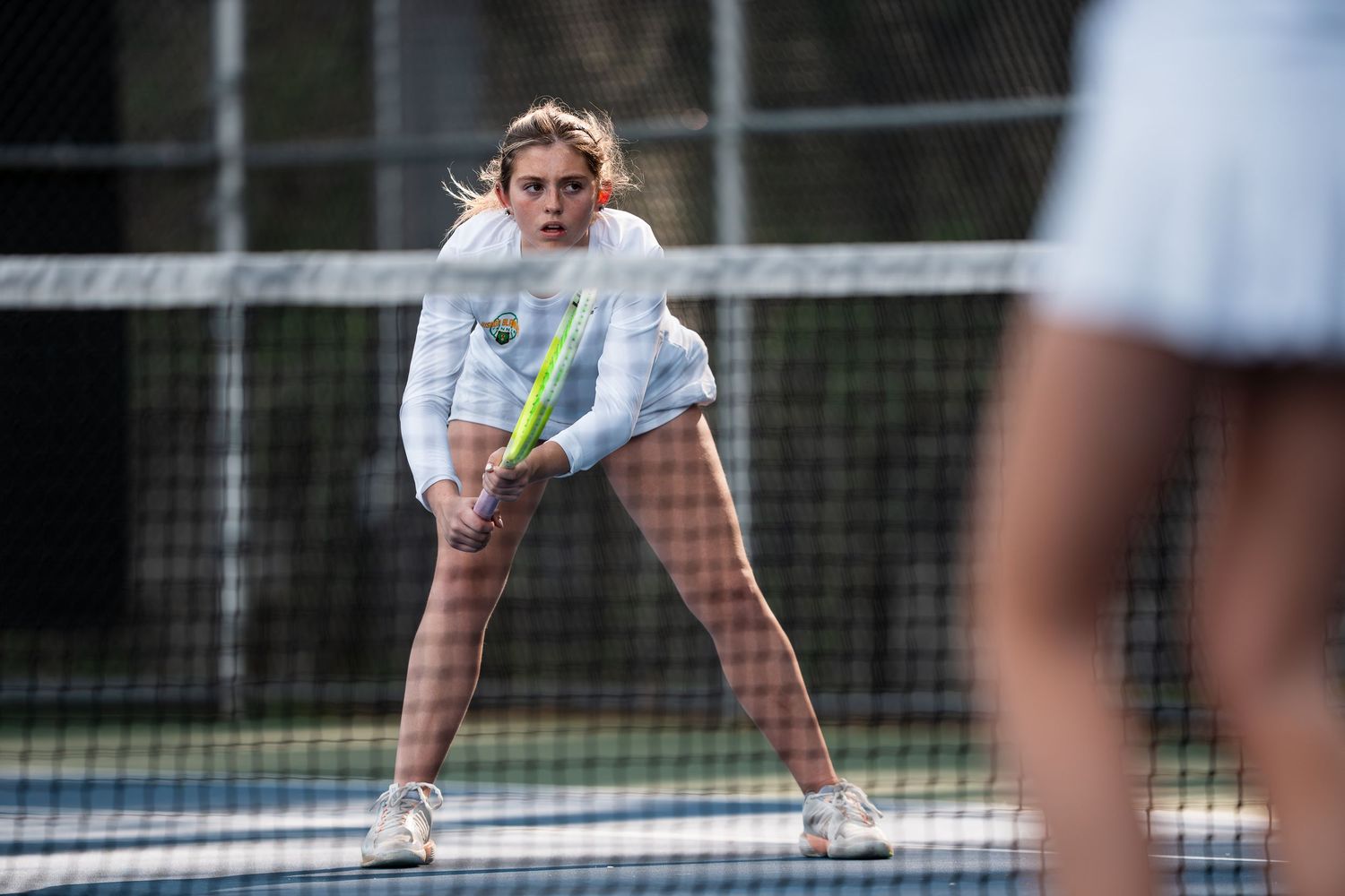 Tennis player crouches in ready position on court while holding racquet during competitive match.