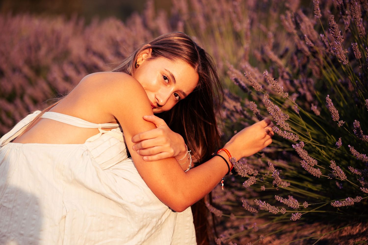 A young woman looks playfully while sitting near lavender bushes during a senior portrait session shot by Carlos Sanchez Photography