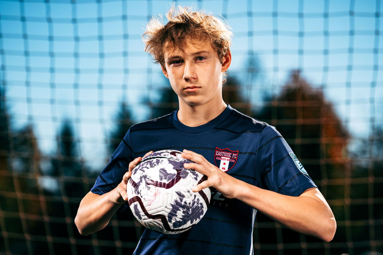 Soccer goalkeeper in blue uniform practices catching drills with a ball against a net background.