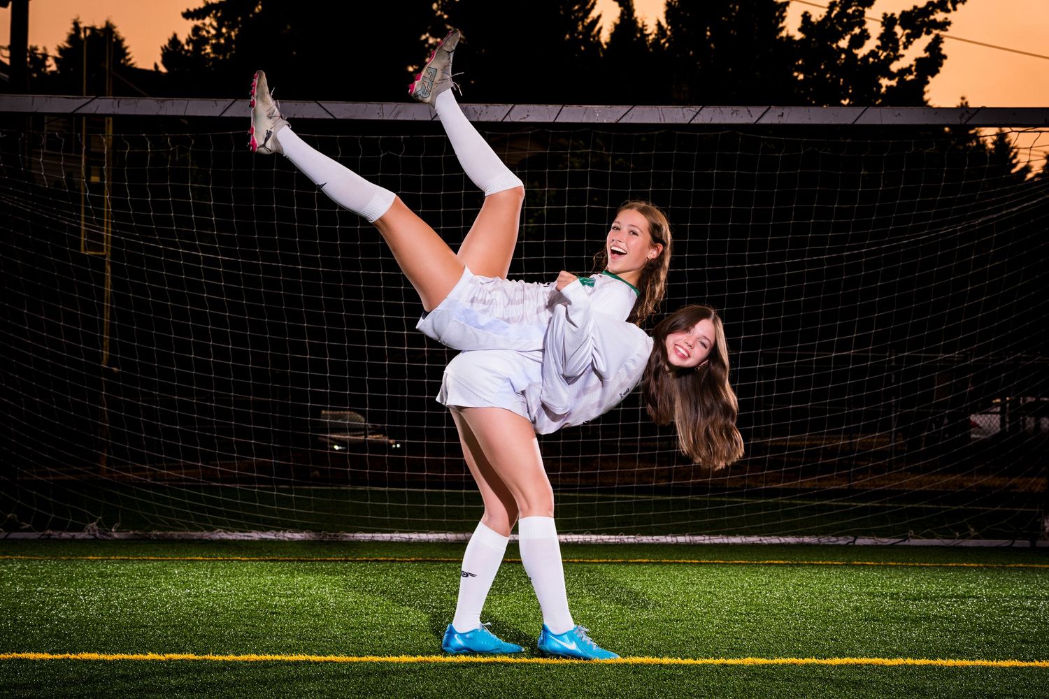 Soccer player performs a high kick on field at dusk with goal net in background.