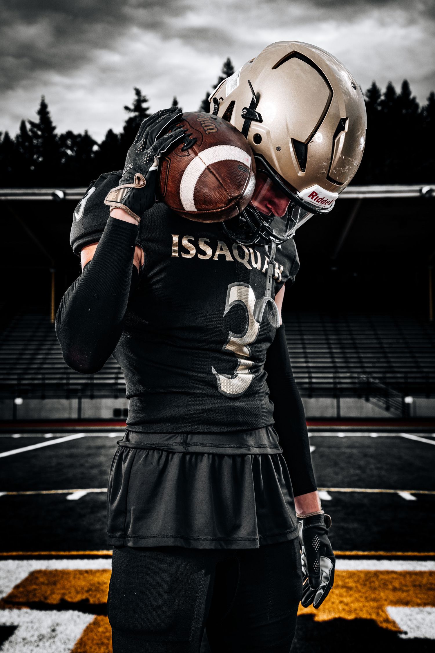 Football players in black Issaquah uniforms huddle together on field at dusk.