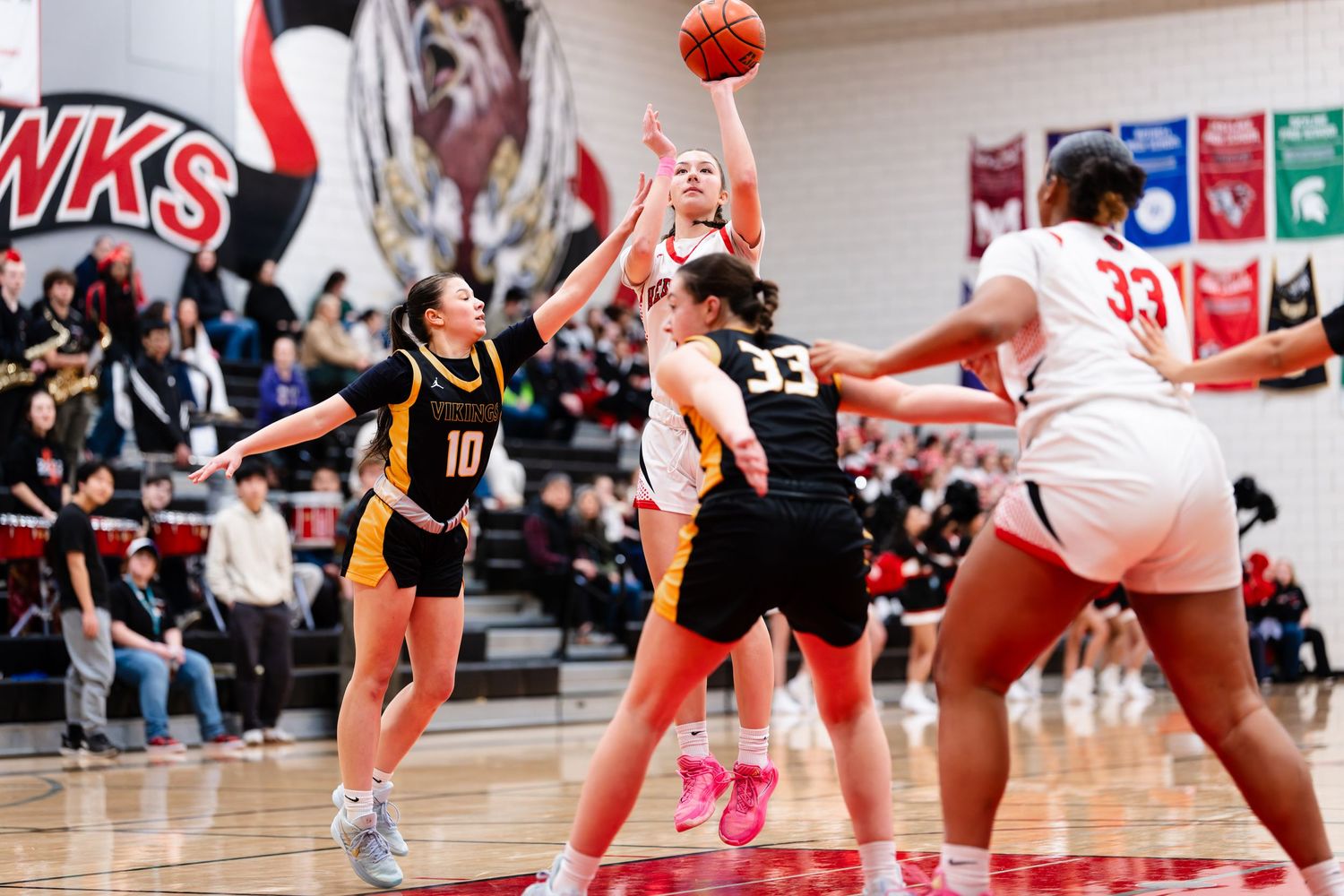 Basketball players in red and black uniforms compete for possession during an intense indoor game.