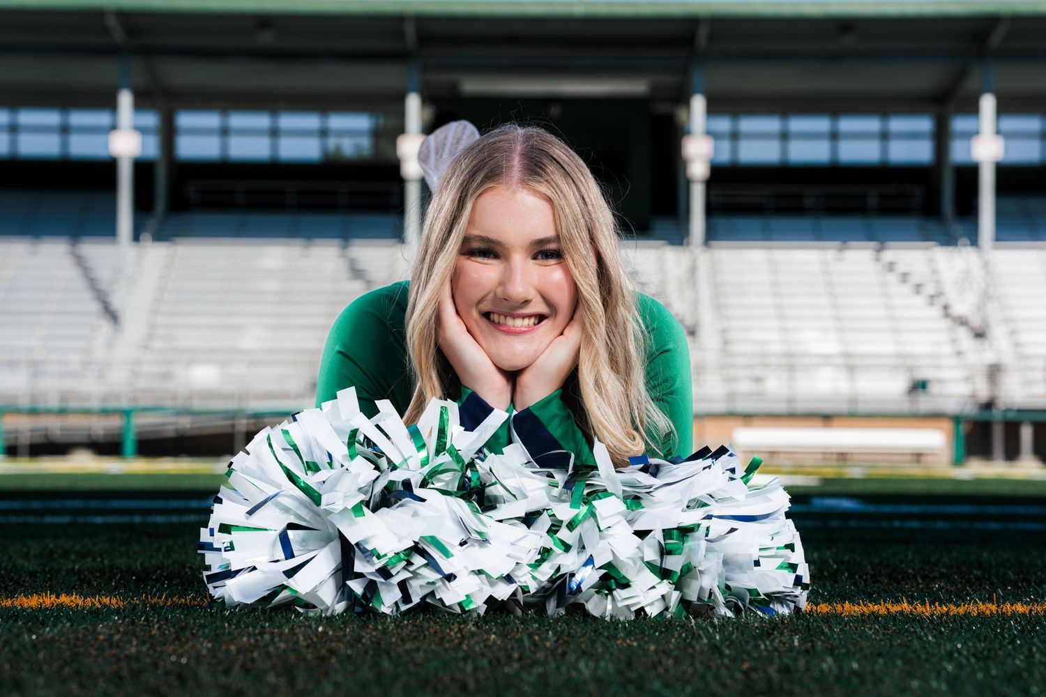 Cheerleader performing poses with pom poms on sports field.