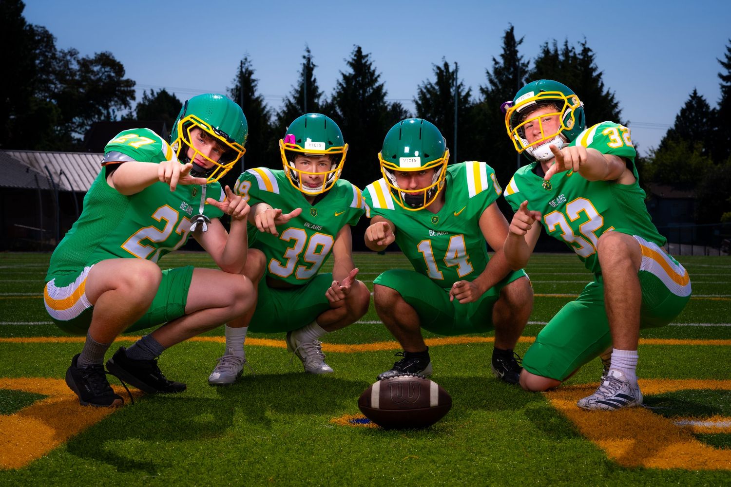 Football players in green jerseys demonstrate proper three-point stance technique during practice drills.