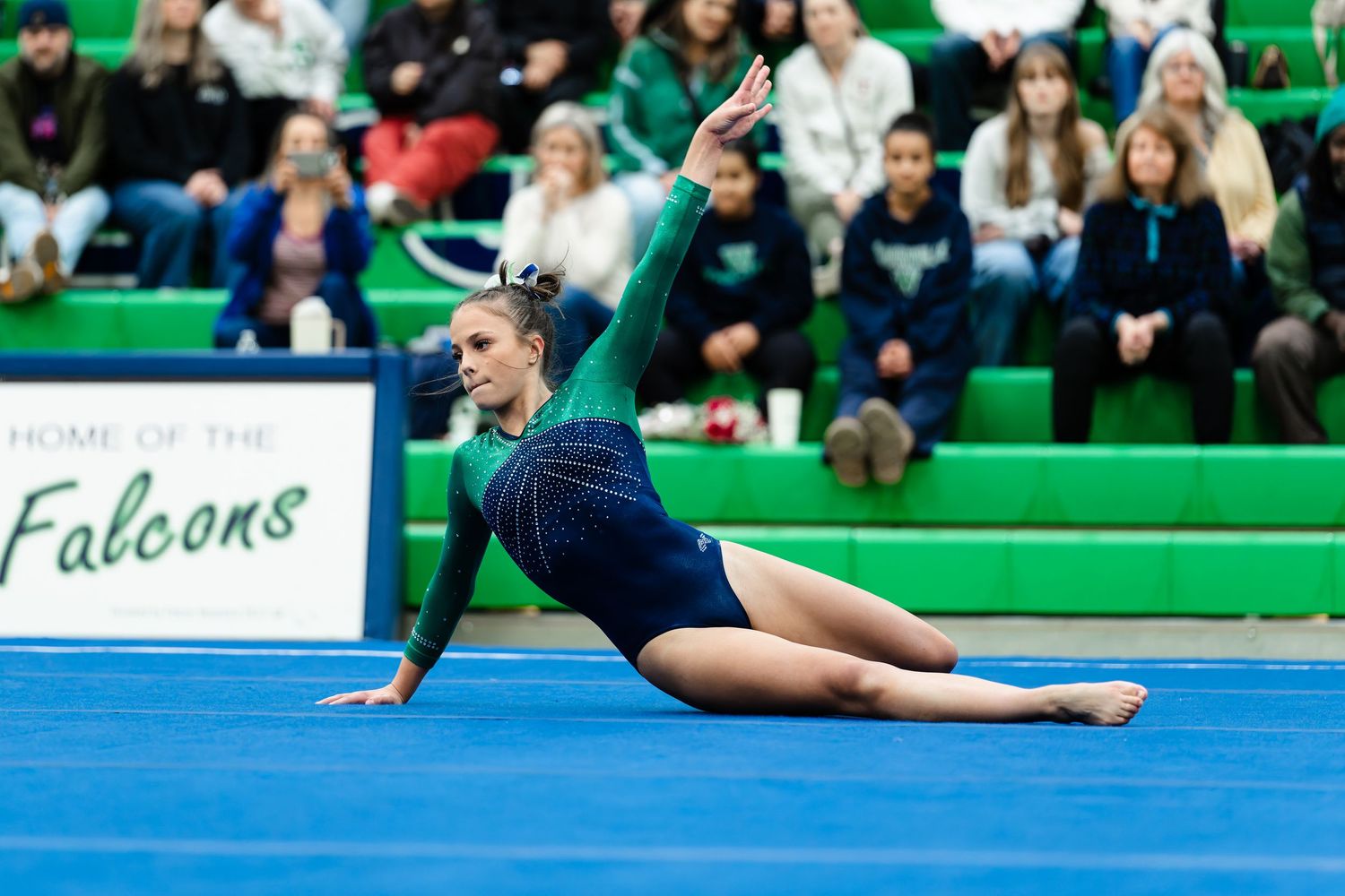 A gymnast performs a graceful floor exercise routine in a blue leotard at a competitive event.