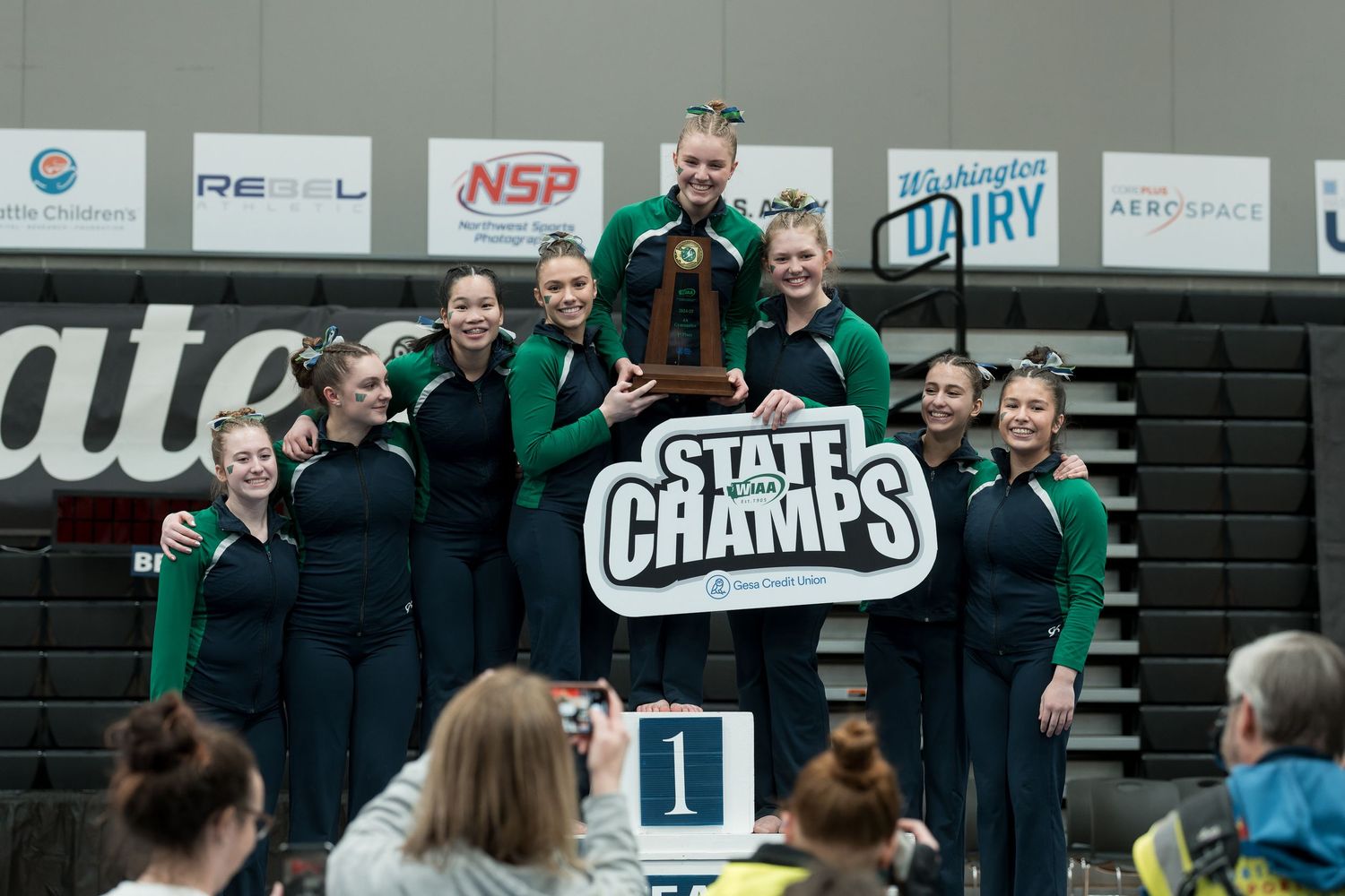 A group of athletes and coaches celebrate together in a gymnasium during a sports event.