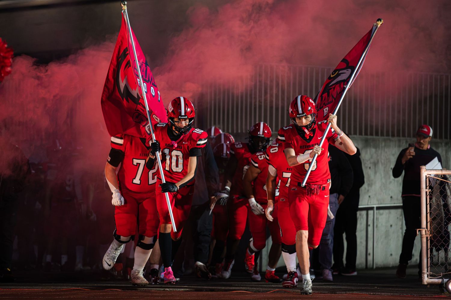 Soccer players in red uniforms celebrate with flares and smoke during a nighttime victory celebration.