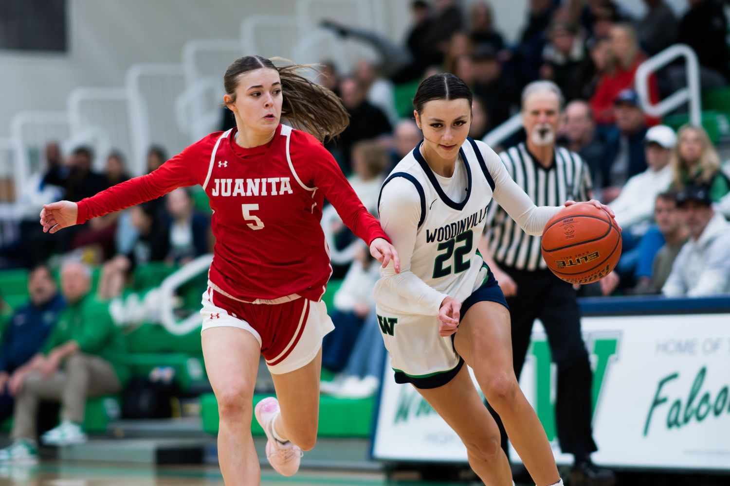 Two basketball players compete during a game with one dribbling down court while the other defends.