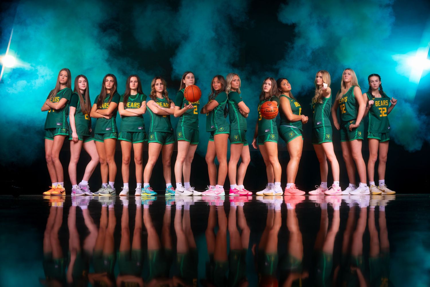 Athletic team poses in matching green uniforms on reflective floor with dramatic teal lighting effects in background.