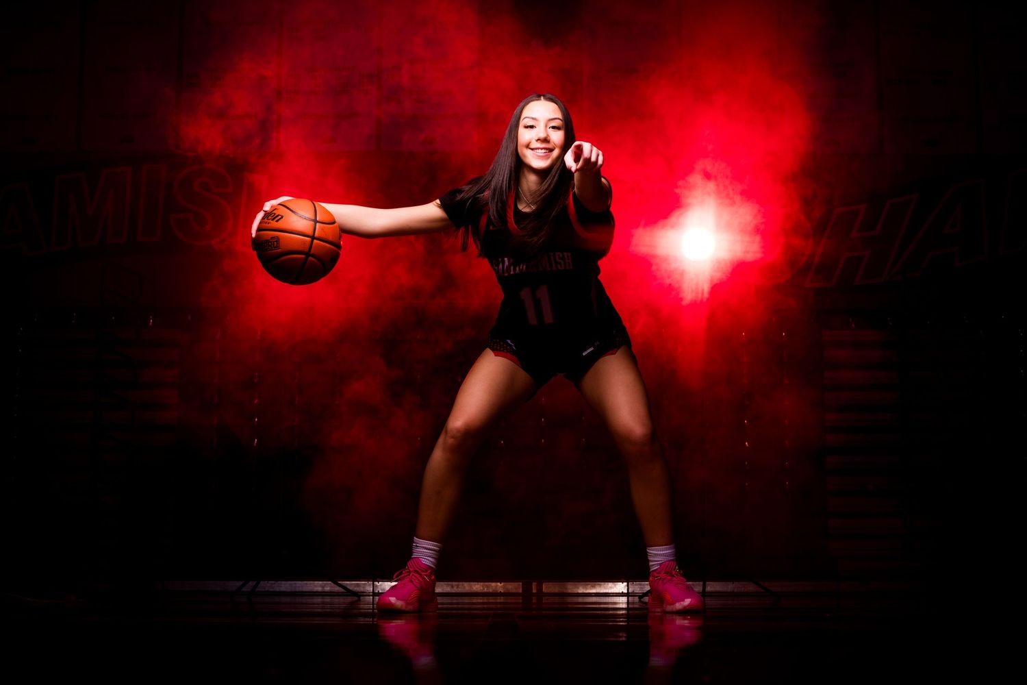 Basketball player in black uniform performs dynamic dribbling move against dark background with red lighting effects.