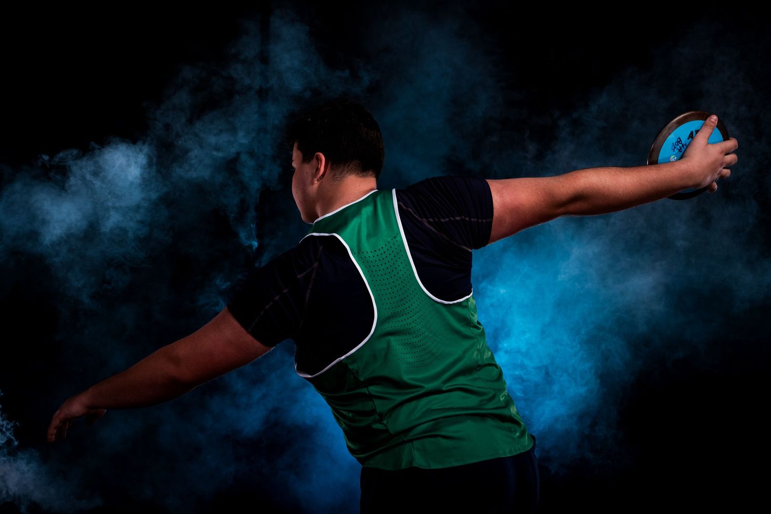 Basketball player in green jersey makes dramatic slam dunk with blue smoke effect in background.