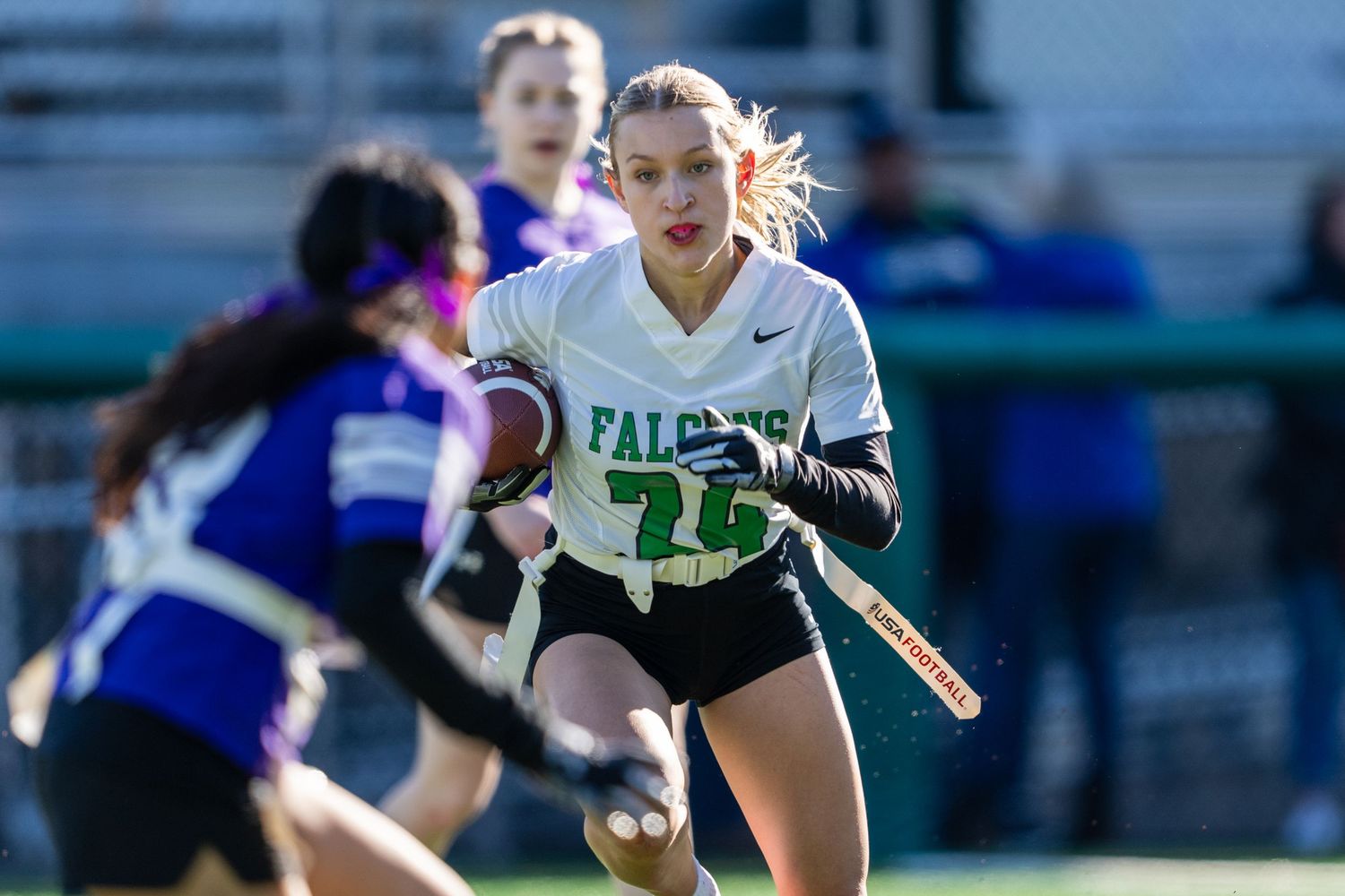 A lacrosse player in a white jersey carries the ball while running down the field during a competitive match.