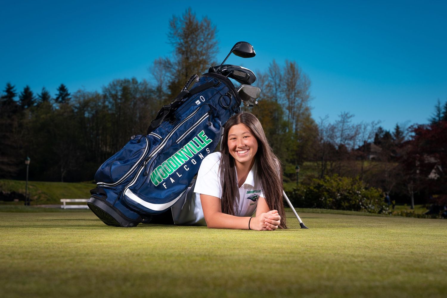 Golf bag lying on green grass field with trees in background under blue sky.