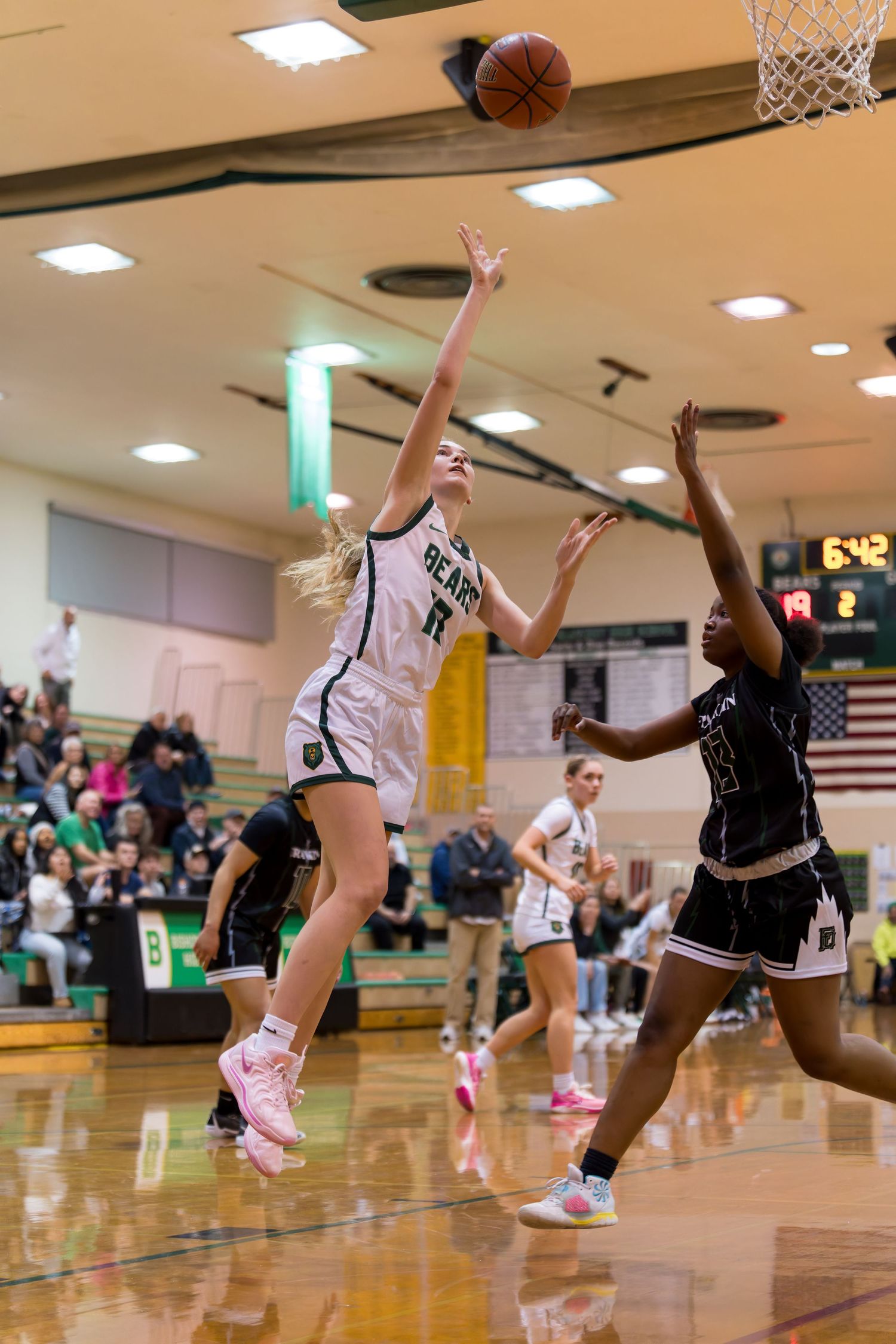 Basketball players compete for the ball during an intense high school game on a polished gymnasium court.