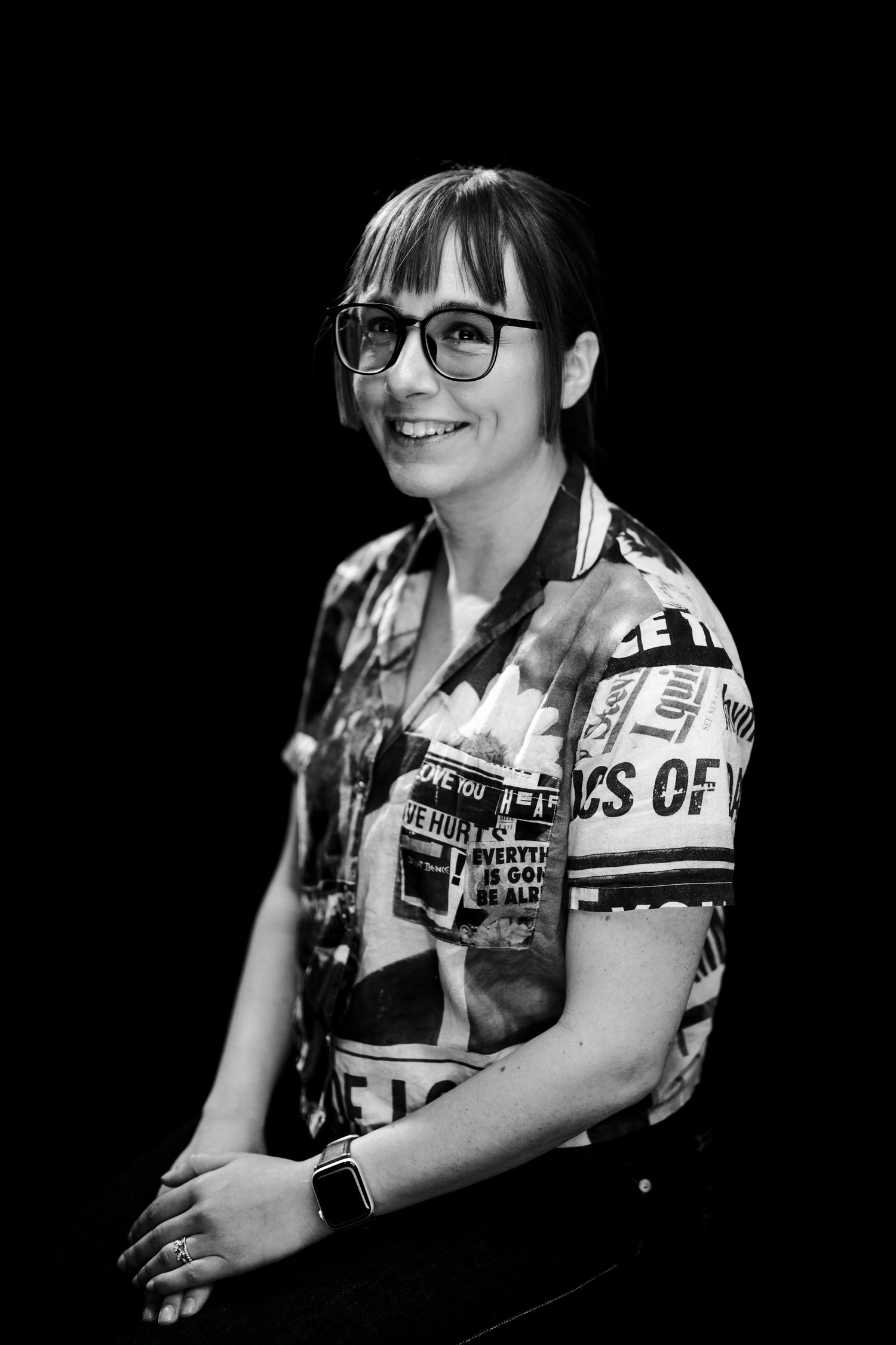 A black and white portrait series showing someone wearing glasses and a vest with text, captured in dramatic lighting.
