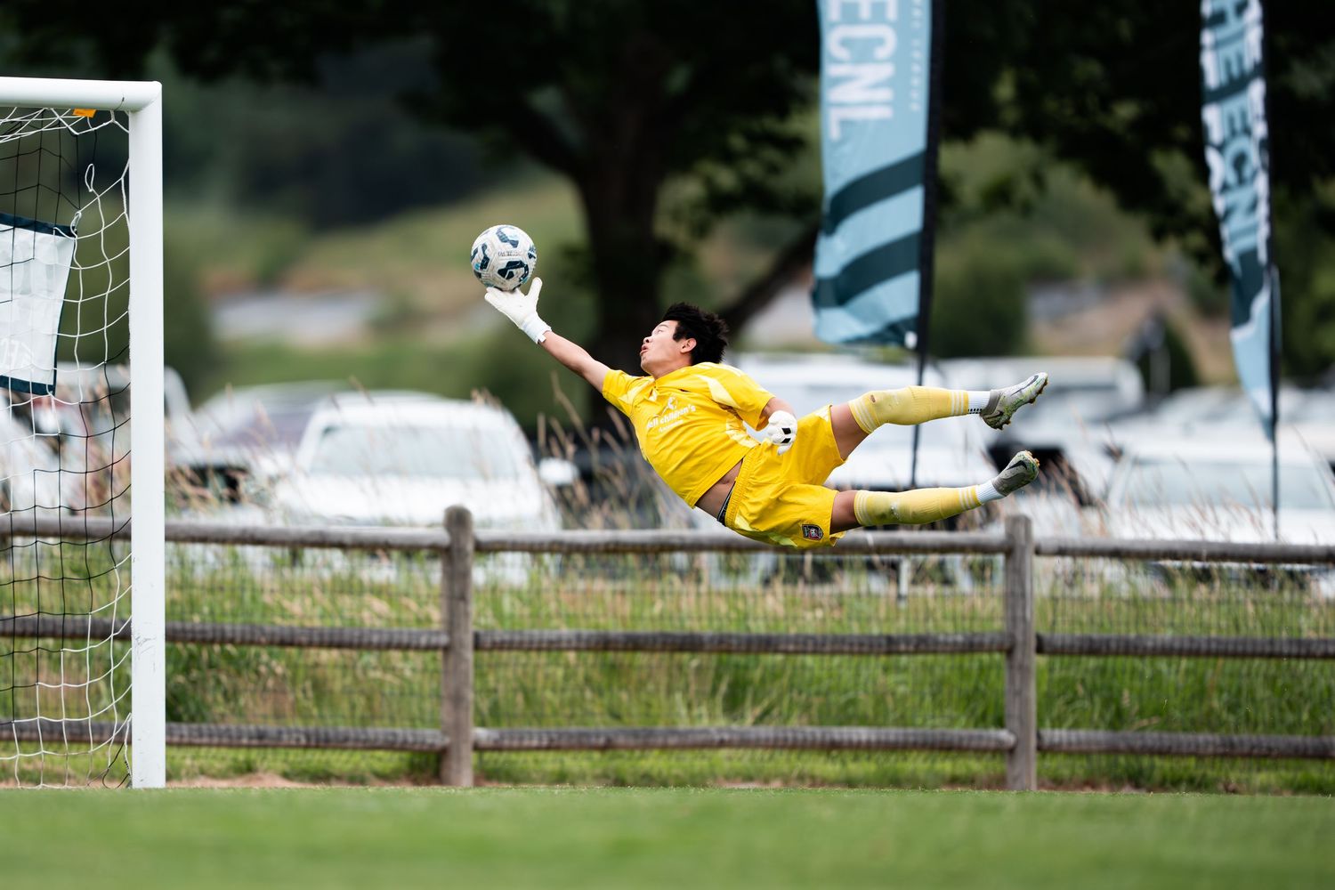 Soccer goalkeeper in yellow uniform makes a diving save attempt during a match on grass field.