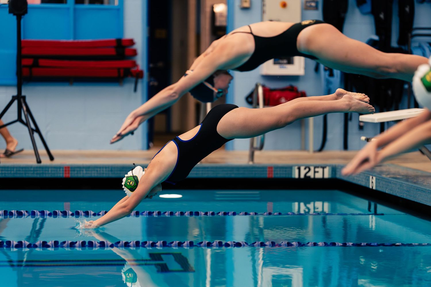 Swimmers in black swimsuits dive gracefully into a pool during a competitive swimming event.