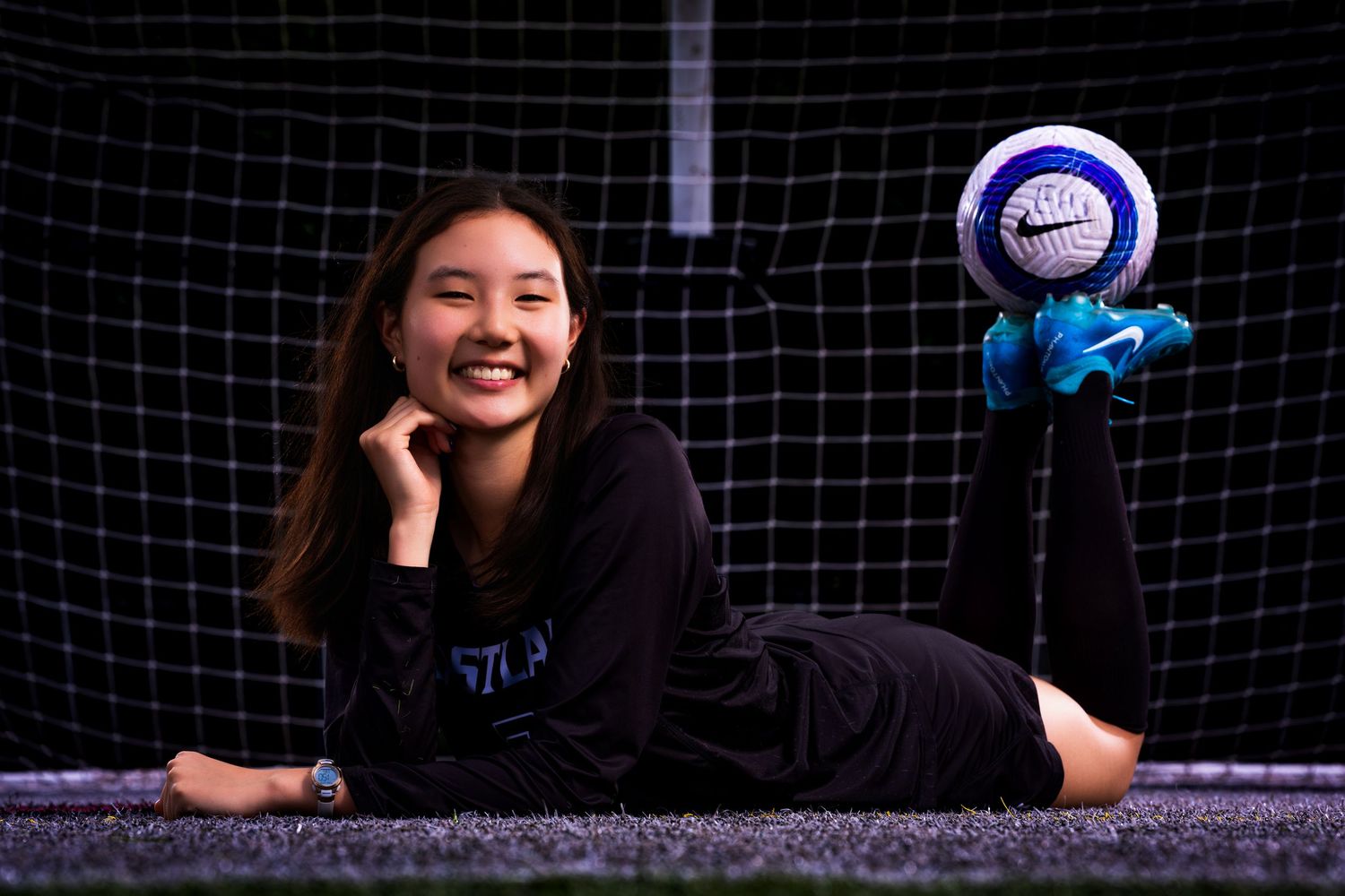 A soccer player poses in front of a goal net with a blue and white ball as a prop.