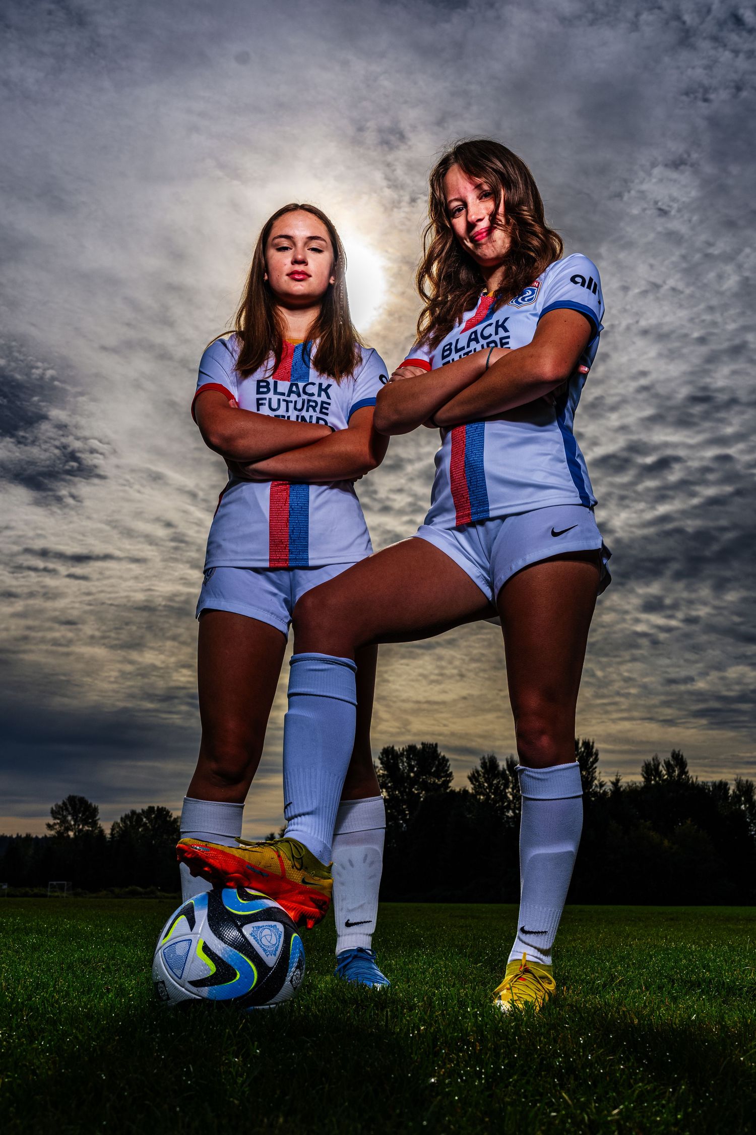 Soccer players pose with a ball against dramatic cloudy sky during a dramatic sunset photoshoot.