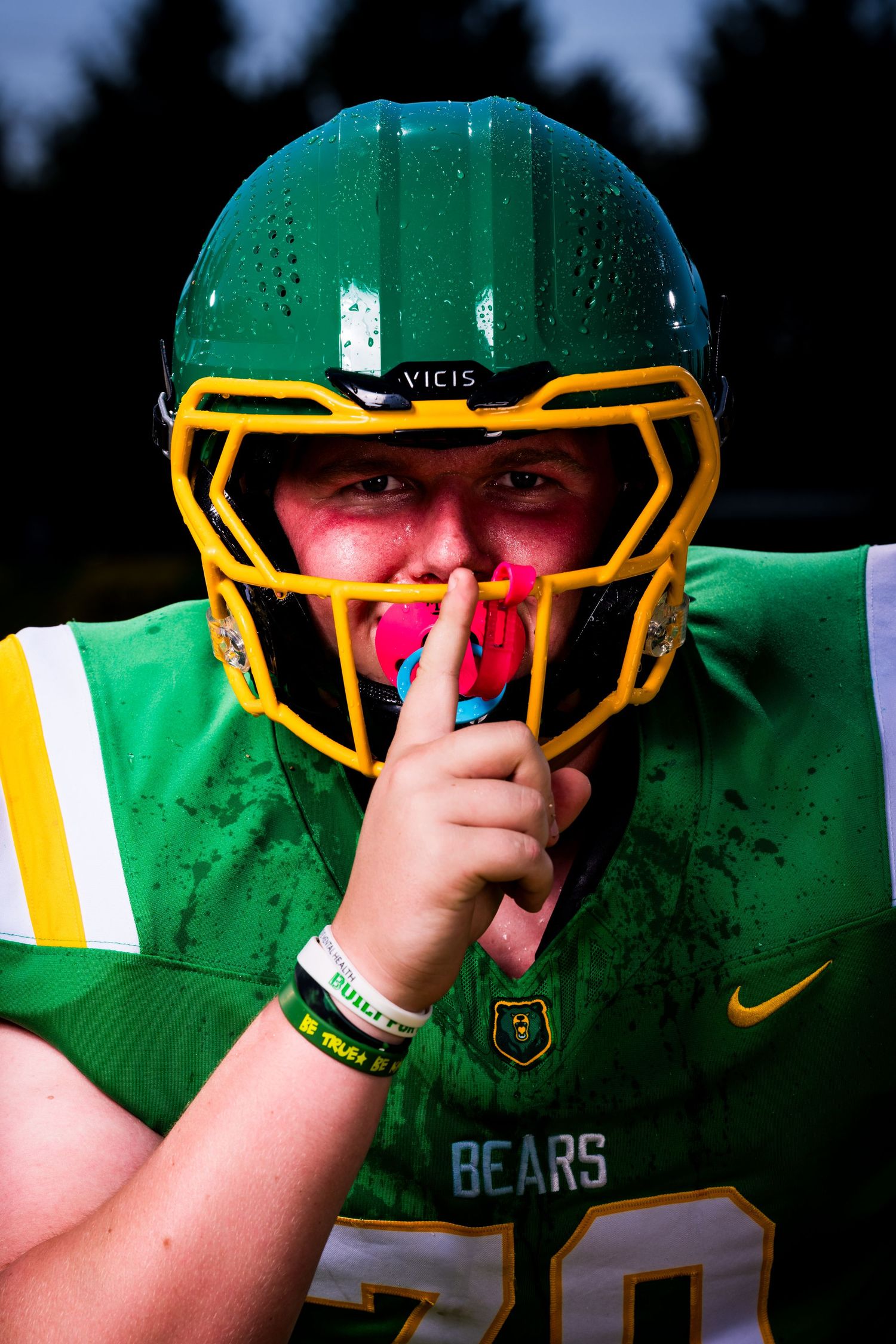 Football player in green and gold helmet making shushing gesture.
