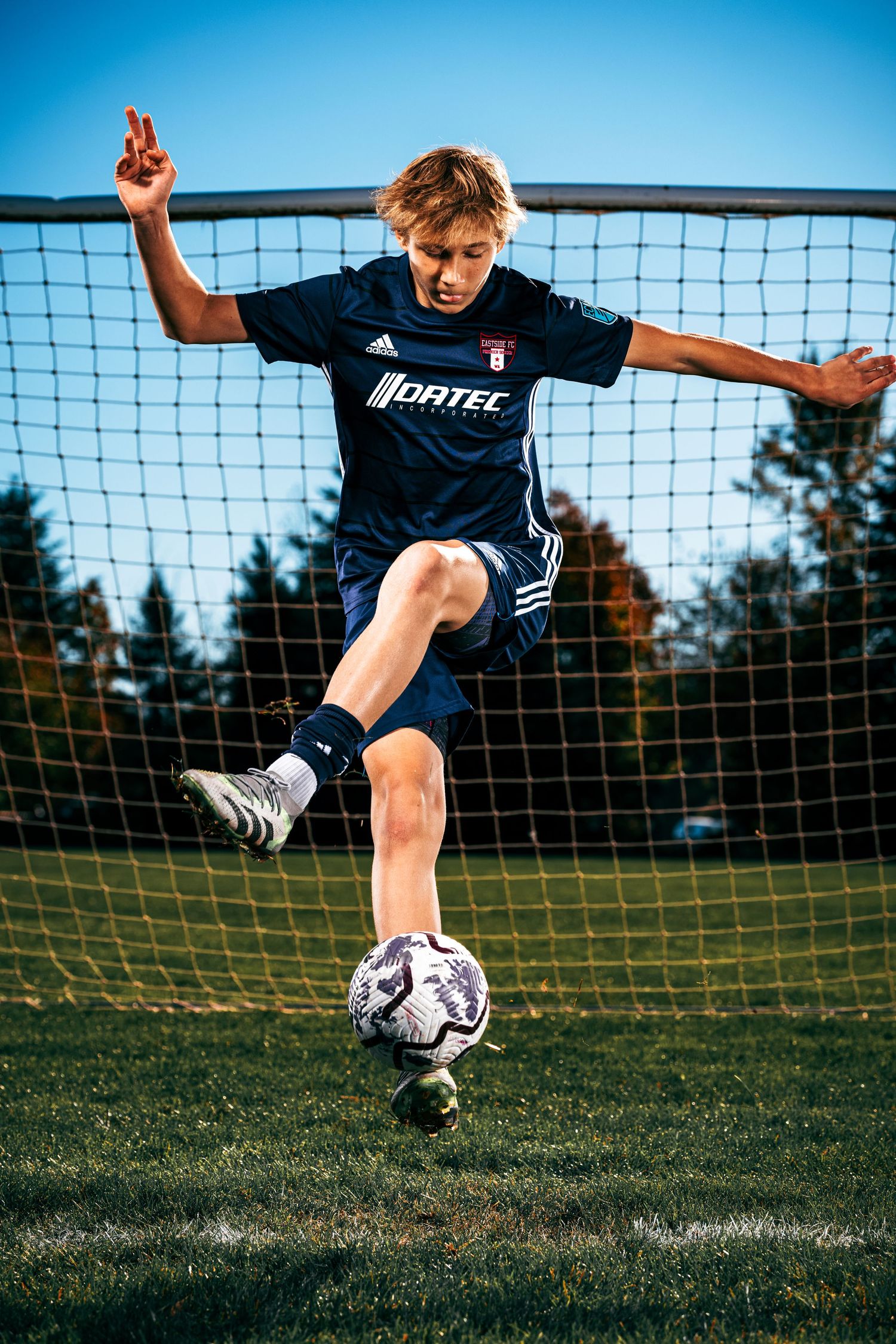 Soccer player practicing penalty kicks at goal with ball and net in outdoor field during sunny day.