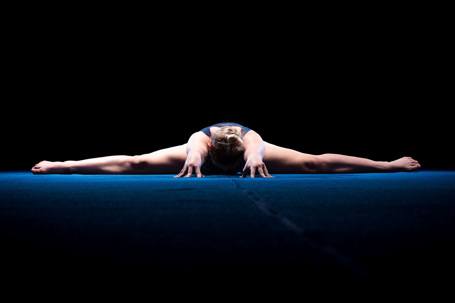 Gymnast performs a split pose on balance beam during artistic gymnastics competition.