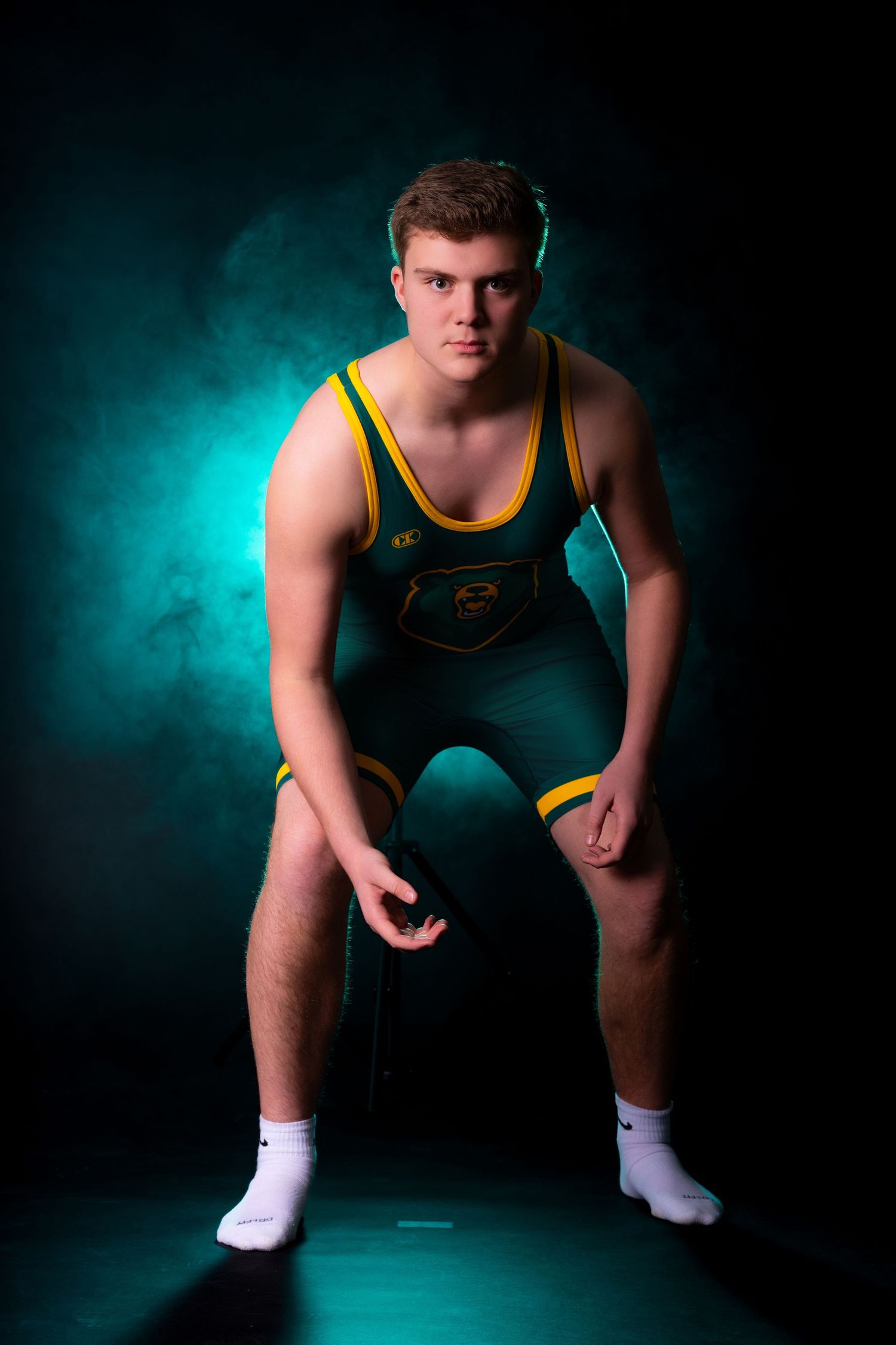 Athlete in green and yellow wrestling singlet poses in dynamic sequence against dramatic teal backdrop with studio lighting.