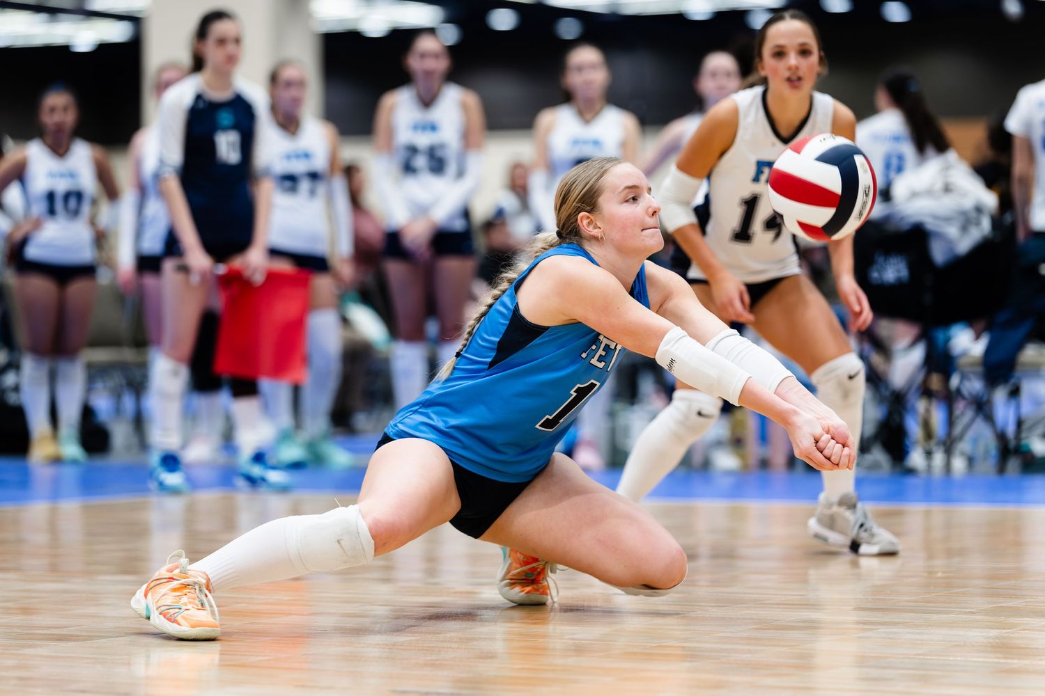 Volleyball players dive and stretch to save the ball during an intense indoor match.