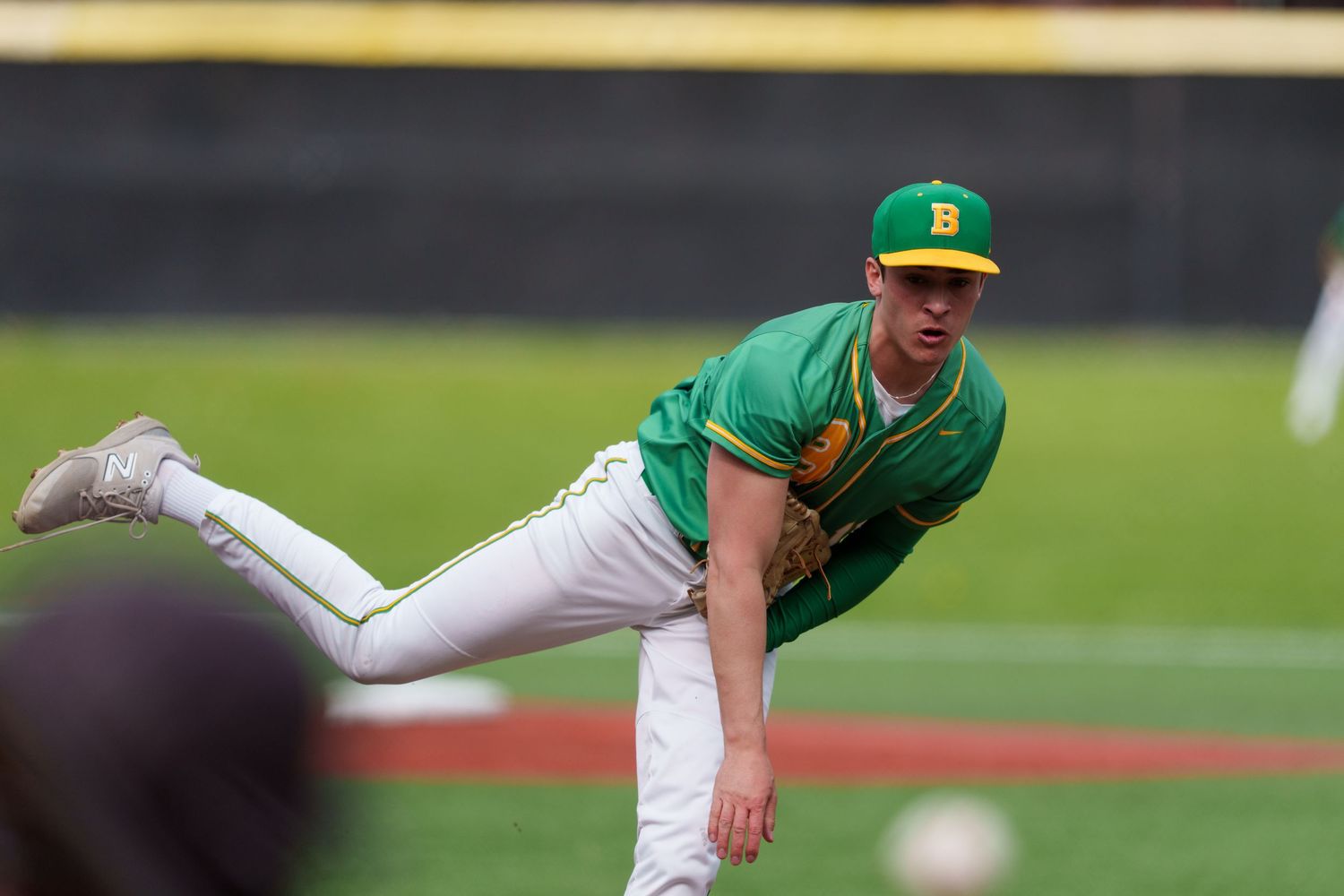 Baseball pitcher in green uniform throws a pitch with dynamic form and motion during game action.