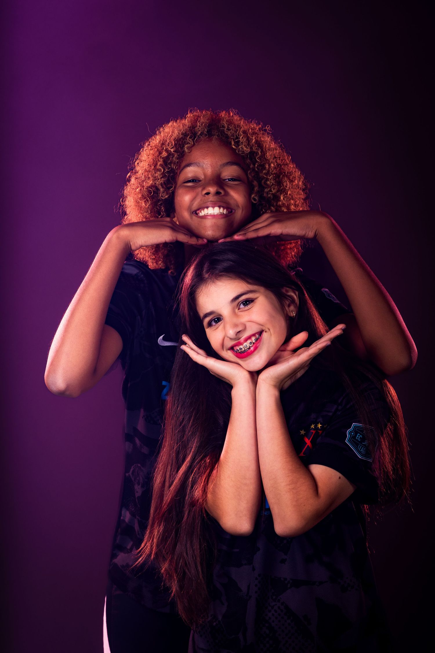 Two friends pose playfully together against purple studio background.
