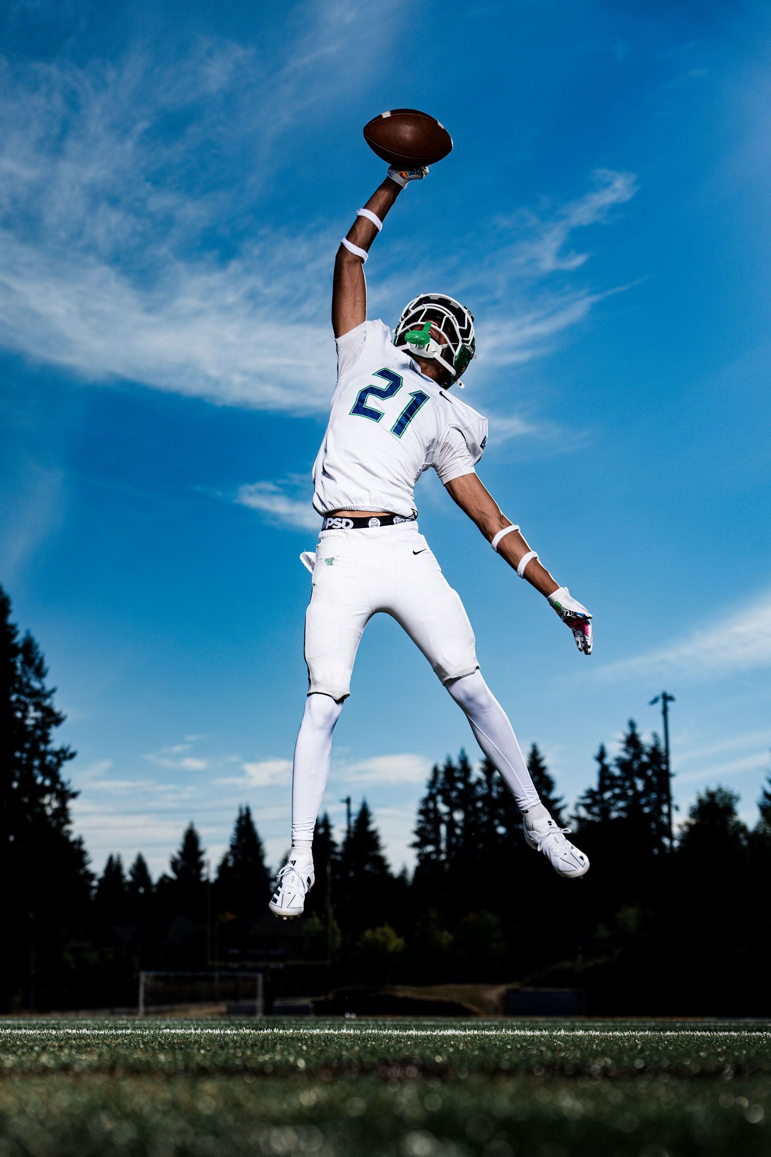 Baseball player makes leaping catch against blue sky and treeline.