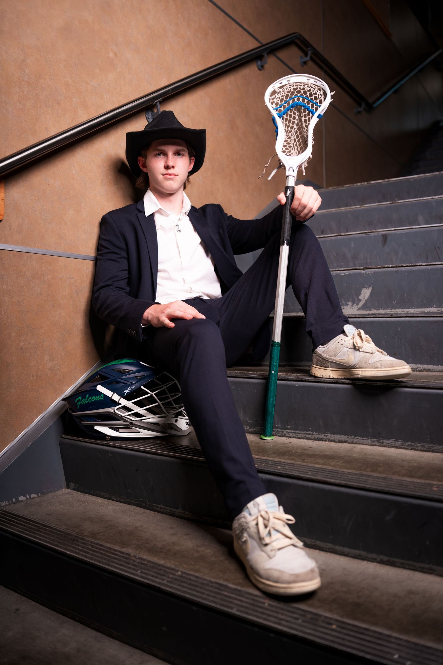 Person in formal black attire sitting on wooden steps with lacrosse stick nearby.