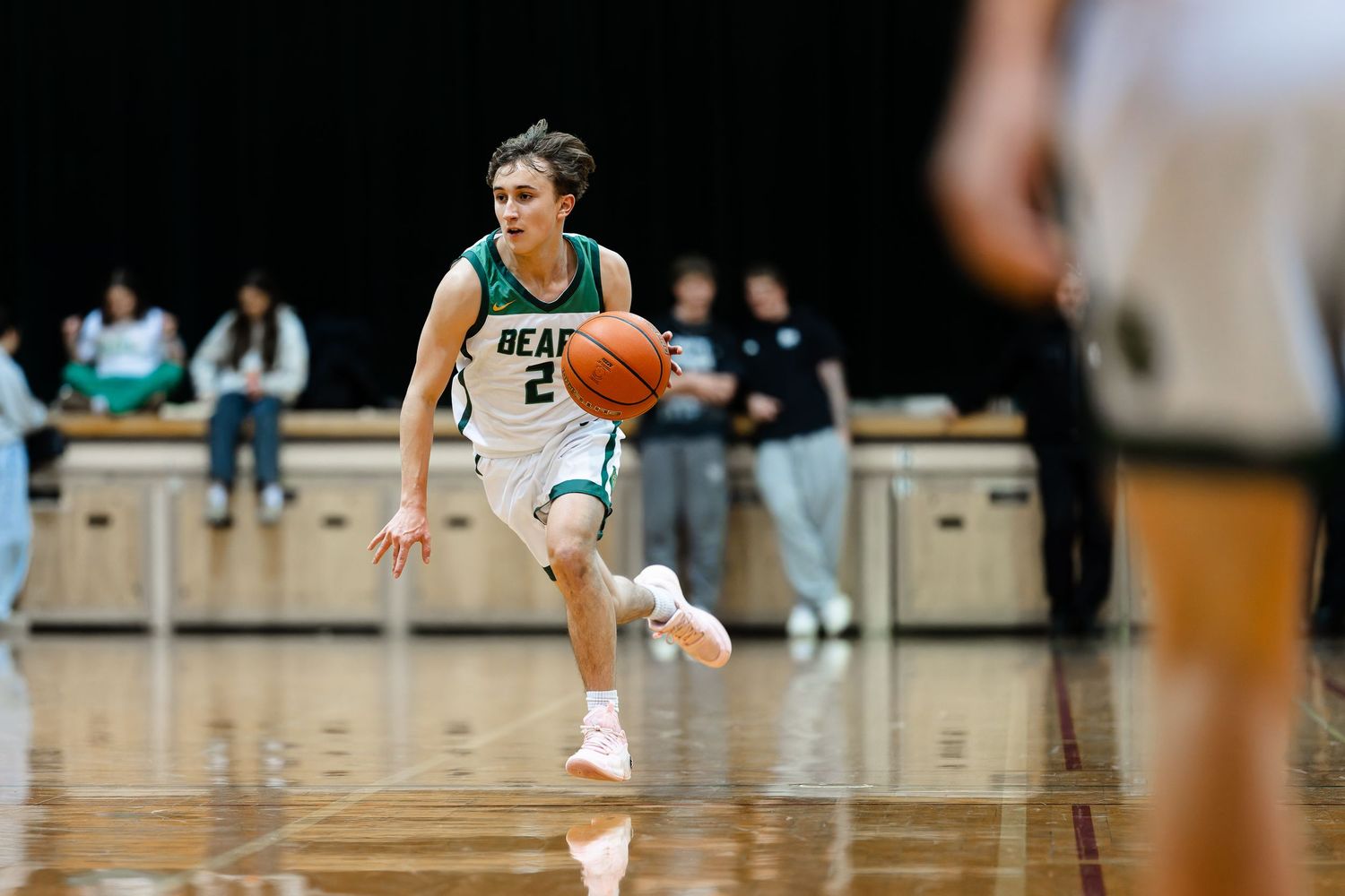 Basketball player in green jersey dribbles down court during competitive game action.