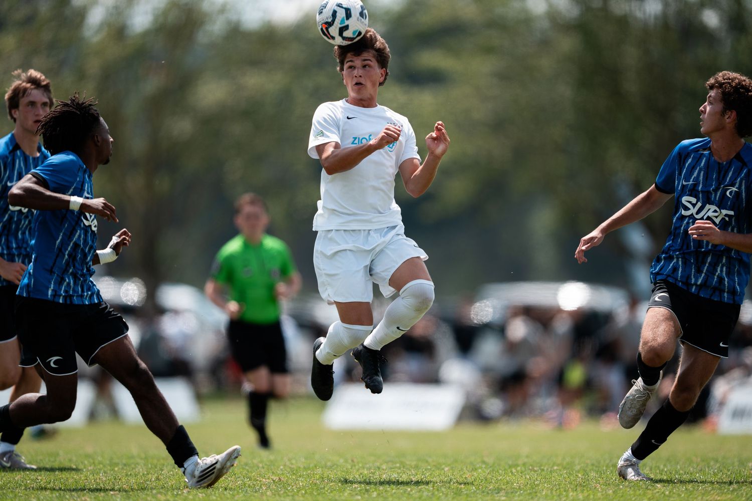 Young soccer players compete for the ball during an intense youth match on a grass field.