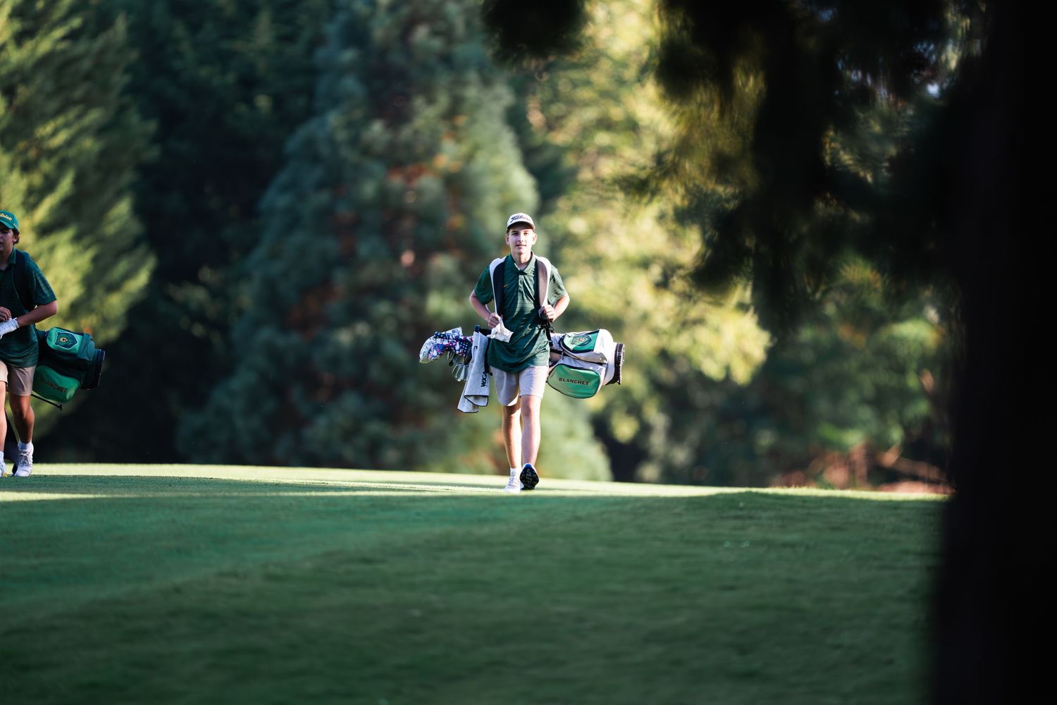 A golfer walks across a sunlit golf course carrying clubs during a warm afternoon round.