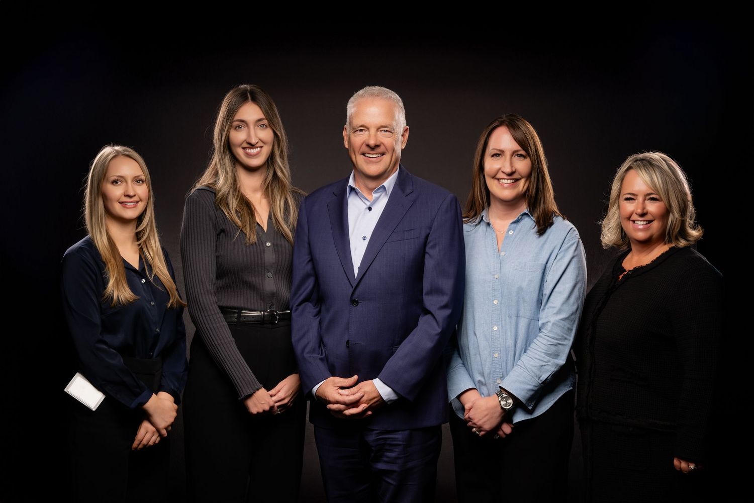 A group of business professionals pose together in formal attire against a dark background.