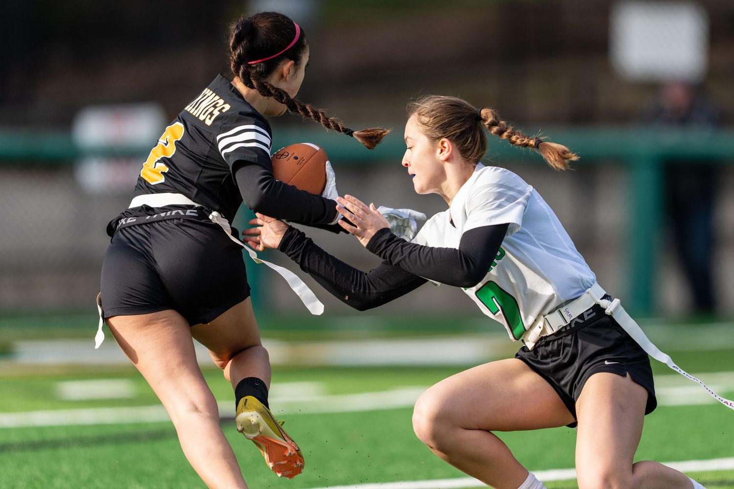 Two flag football players compete for the ball during an intense defensive play on the turf field.
