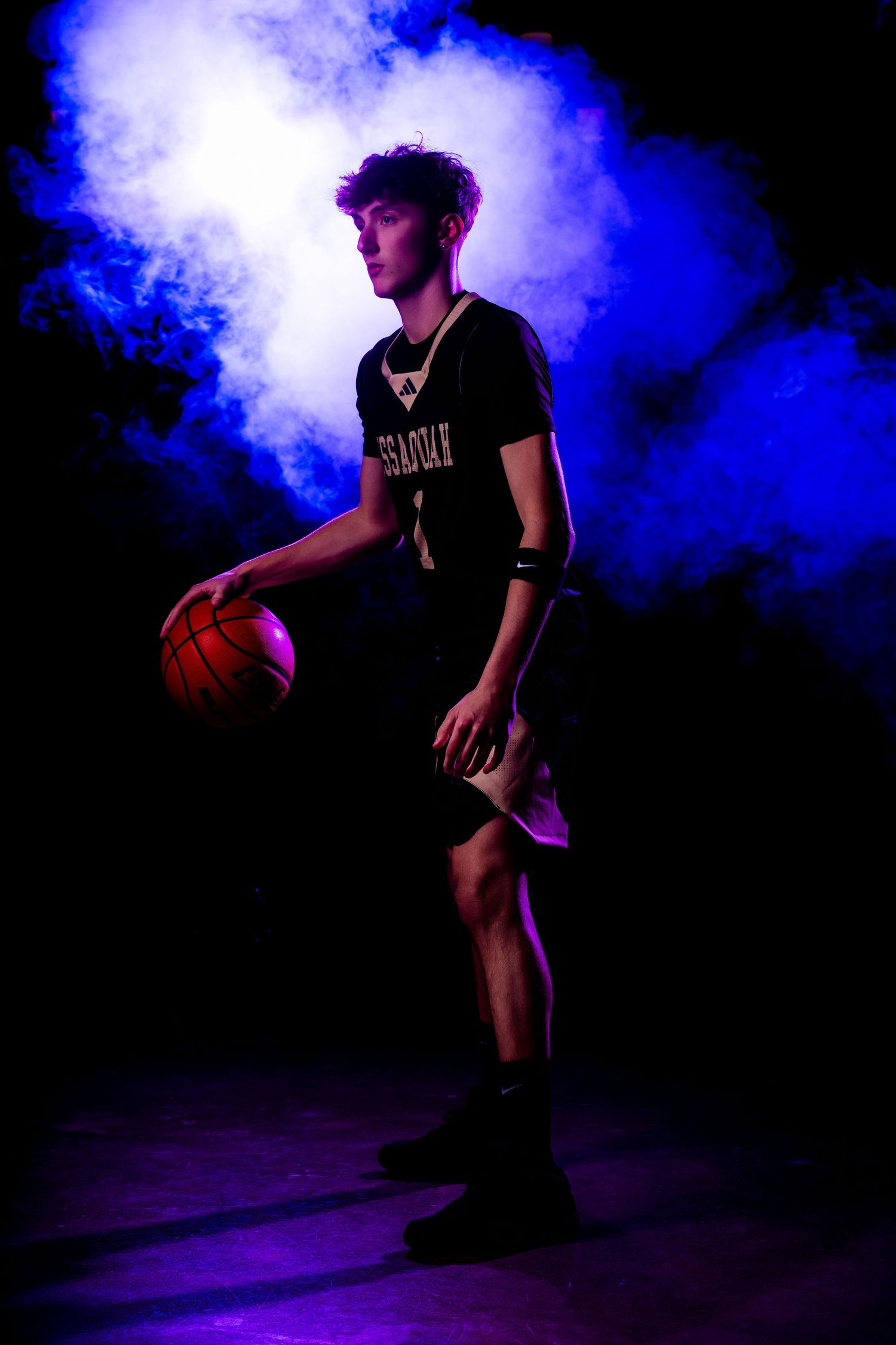 Basketball player silhouetted against dramatic blue smoke effects during dynamic performance on dark stage.
