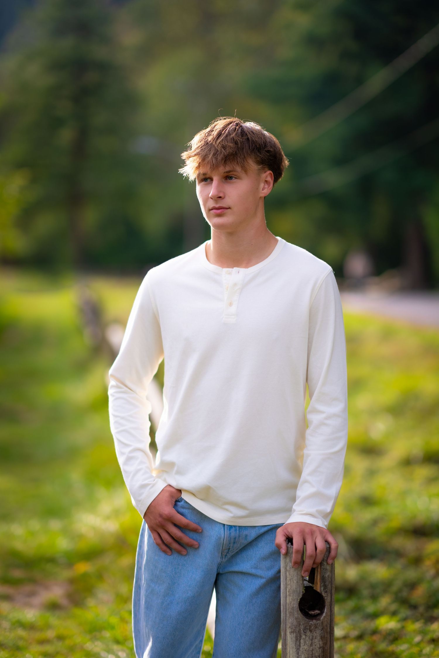 Casual portrait of young person in white sweater and jeans against blurred natural background.