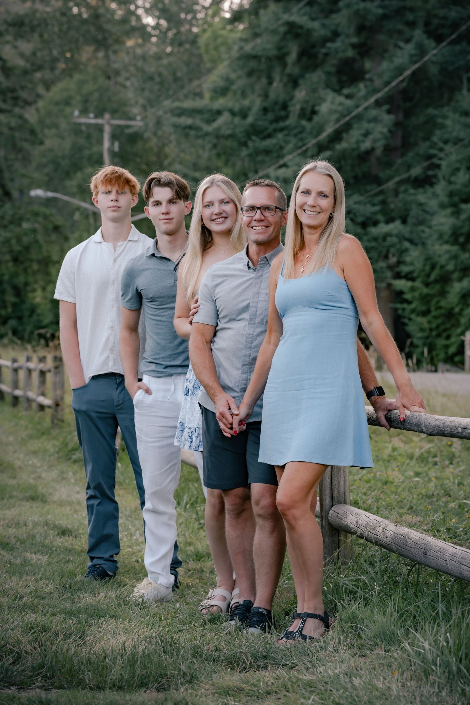 Group of people standing together outdoors along a wooden fence in casual summer attire.