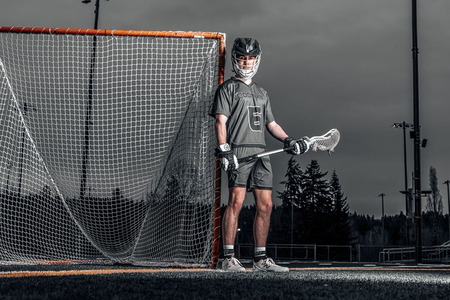 Lacrosse players practice drills near goal net during overcast evening session.