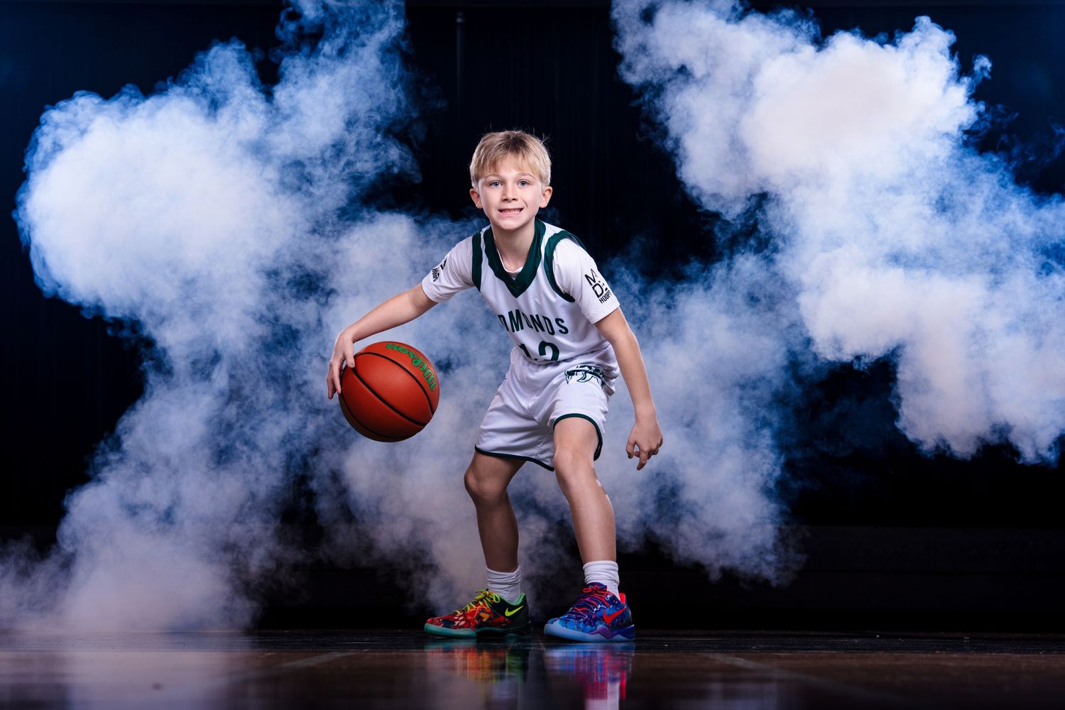 Basketball player emerges dramatically through smoke effects on dark court during team introduction.