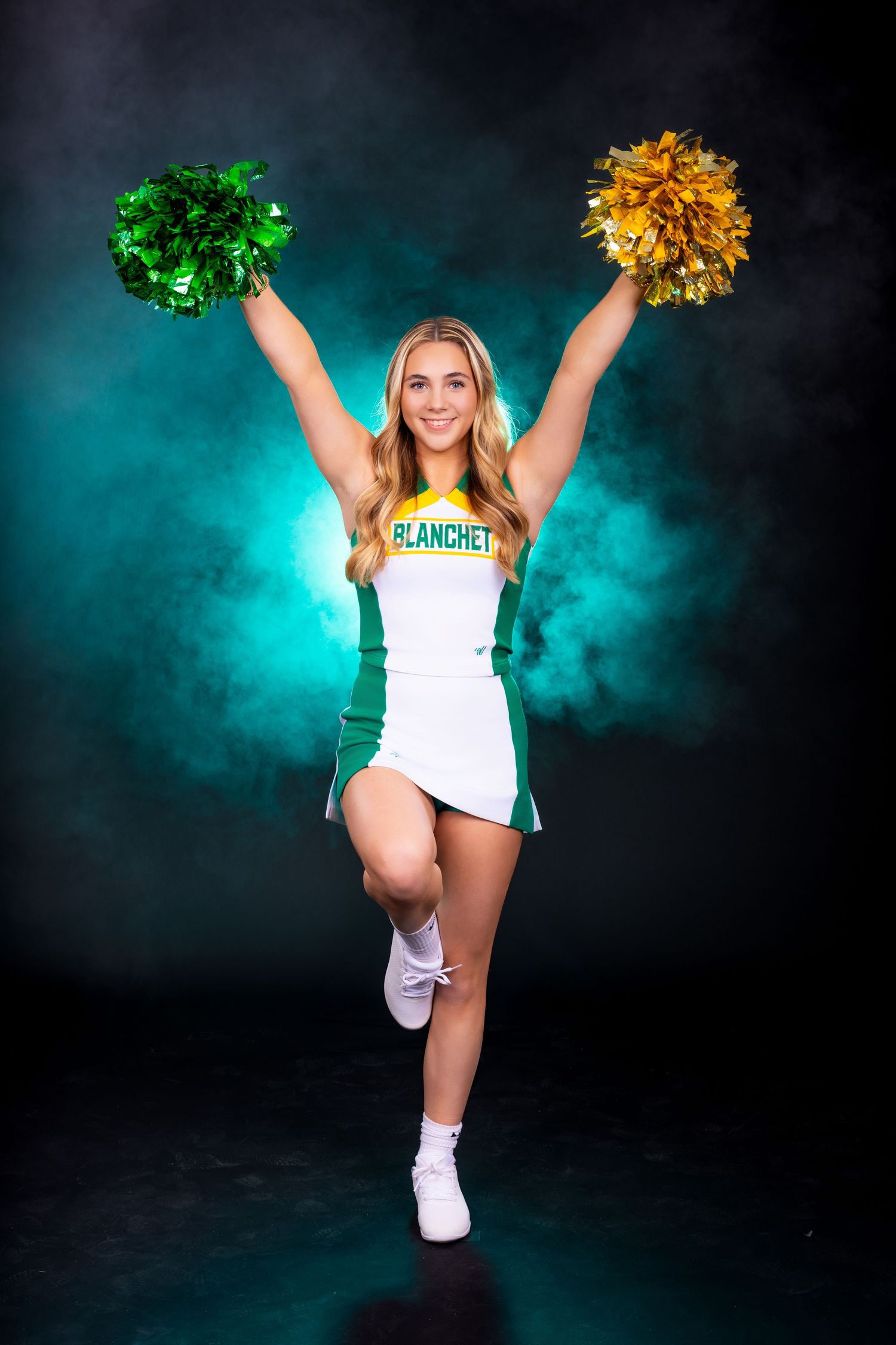 A cheerleader in green and white uniform jumps energetically with gold and green pom poms against a teal smoky background.