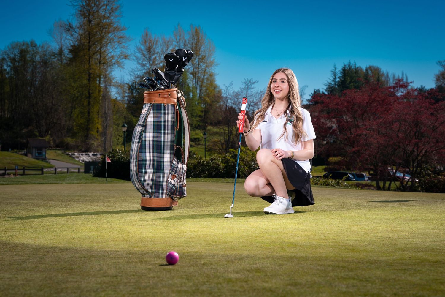 A golfer practices putting on a sunny day at a golf course with multiple views of the green.