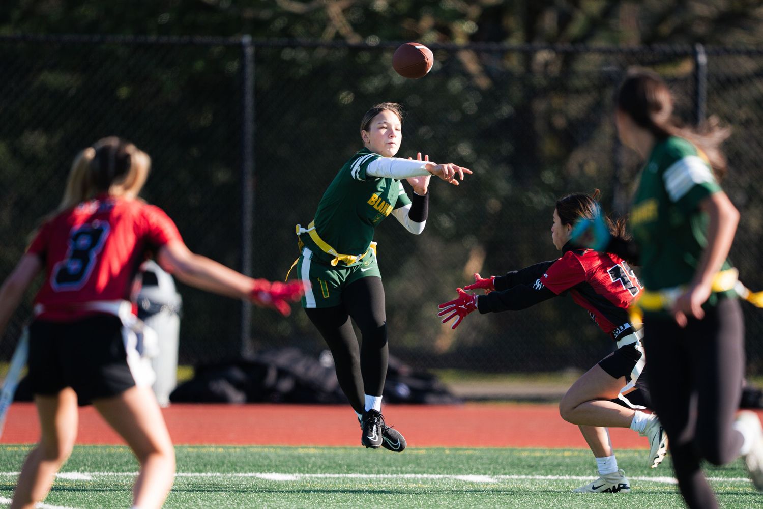 Flag football players compete on a sports field as someone leaps to catch a pass during an intense game.