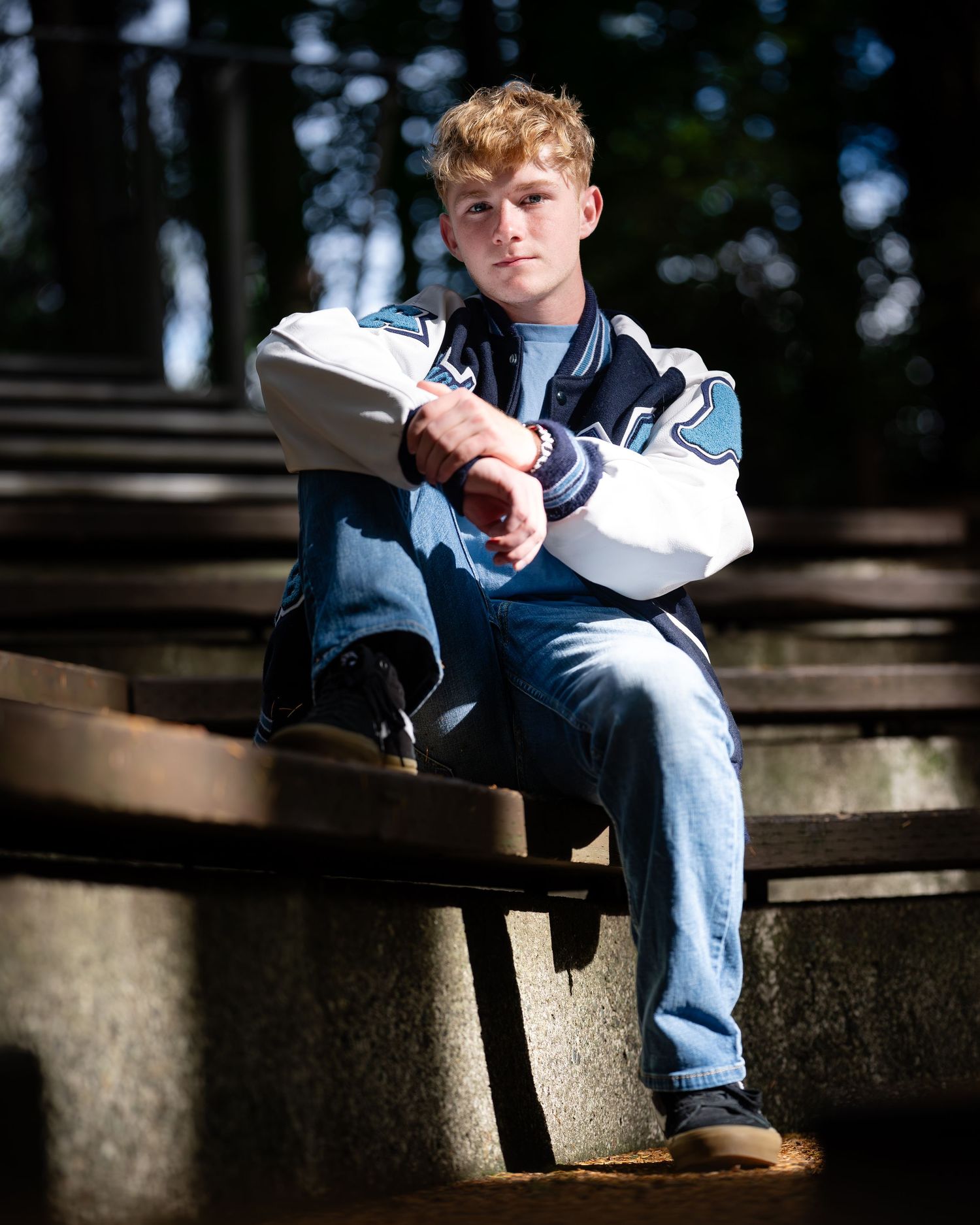 Person sitting on wooden steps in casual attire with blue jeans and a baseball cap in natural outdoor lighting.