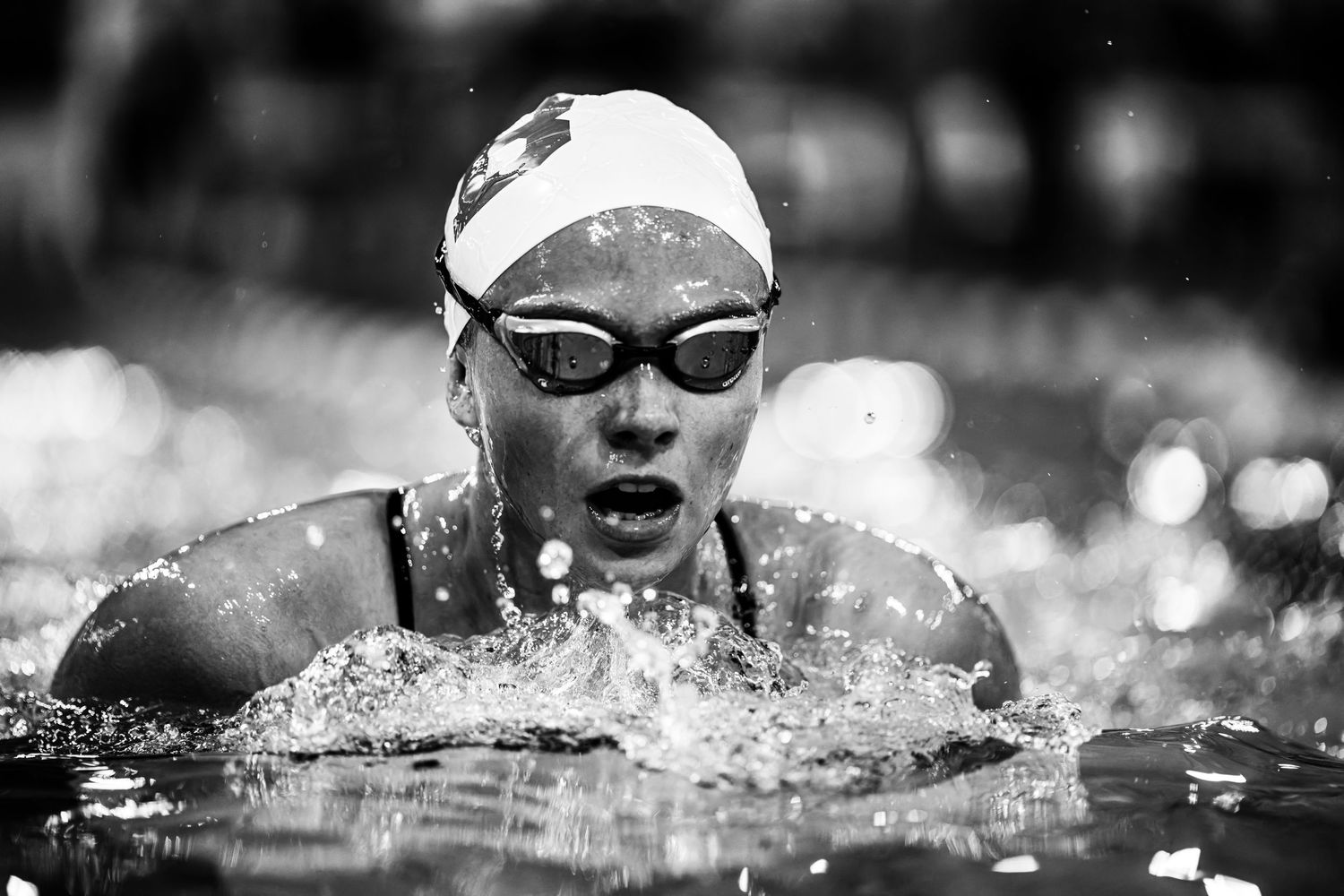 A sequence of competitive swimmers racing in a pool captured in black and white photography.