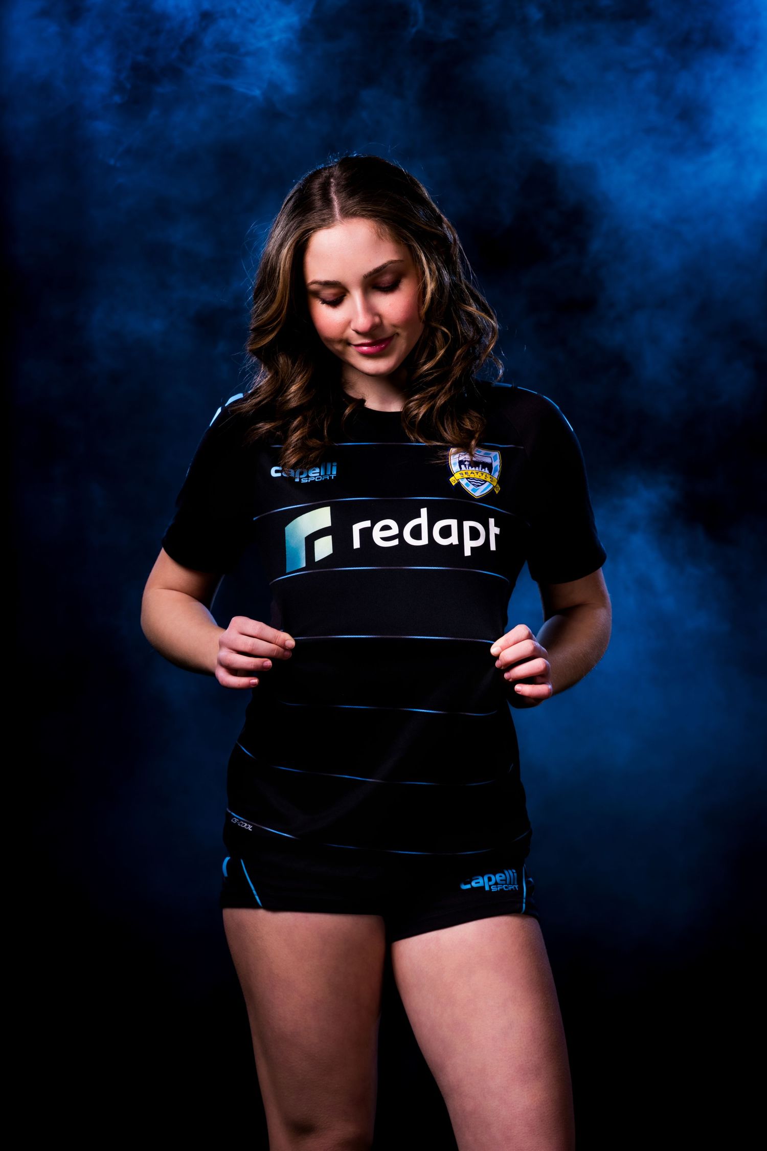 Athletic model in black sports uniform with Redapi sponsor logo poses against dramatic blue smoky background.