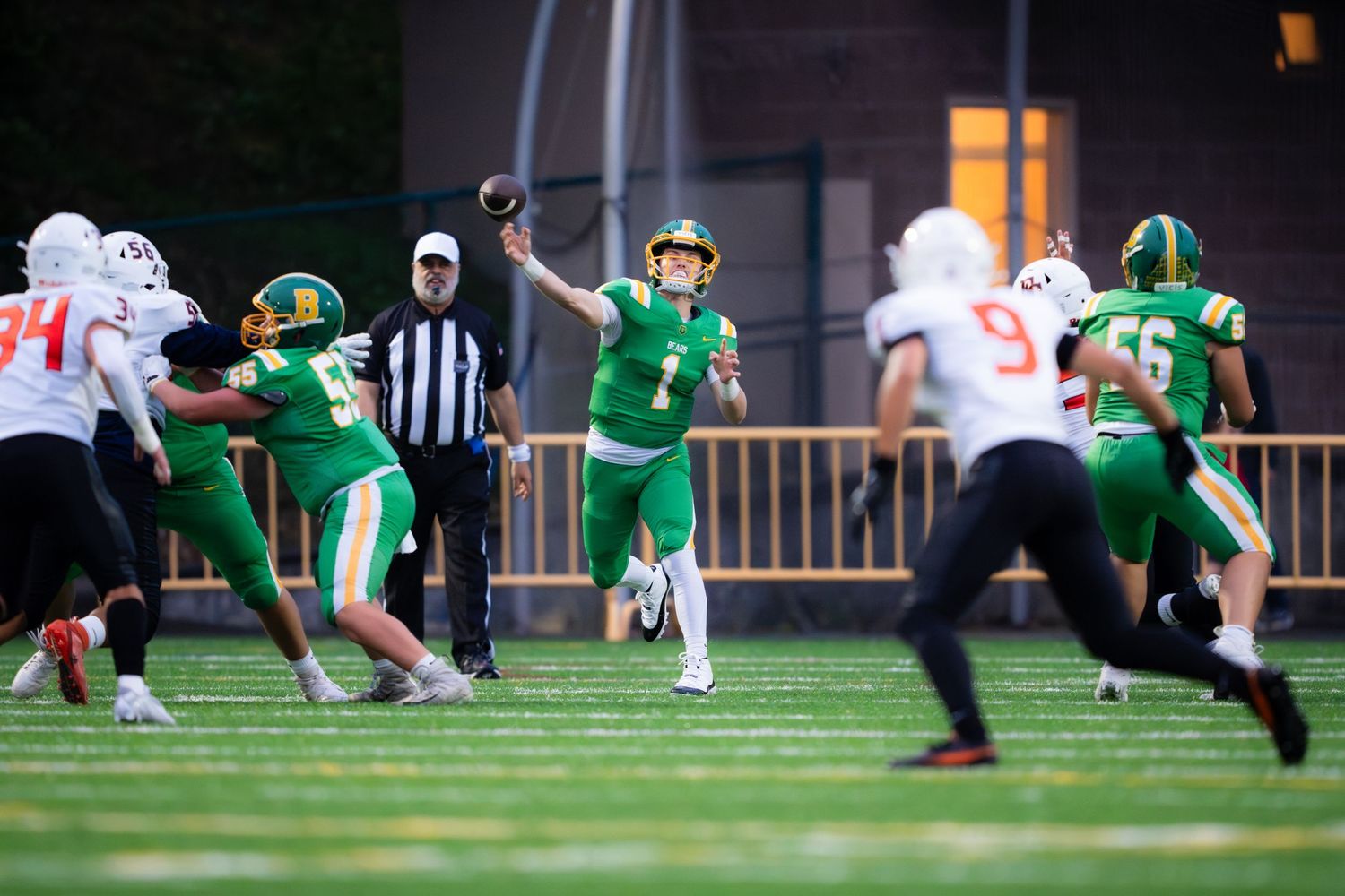 A football player in green jersey makes a diving catch during a game against players in white uniforms.