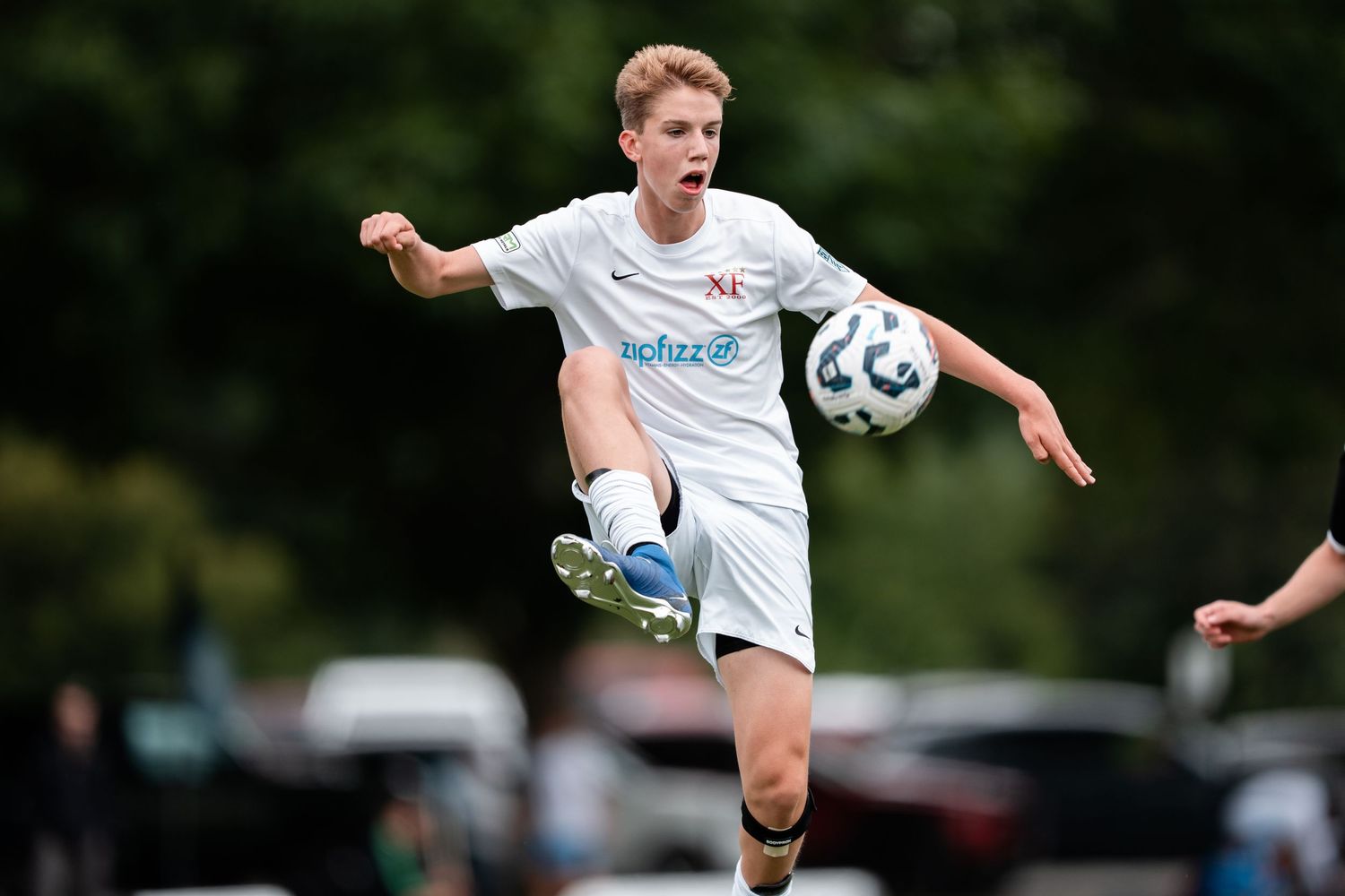 Soccer player in white uniform performs a high kick during an outdoor match on a grass field.